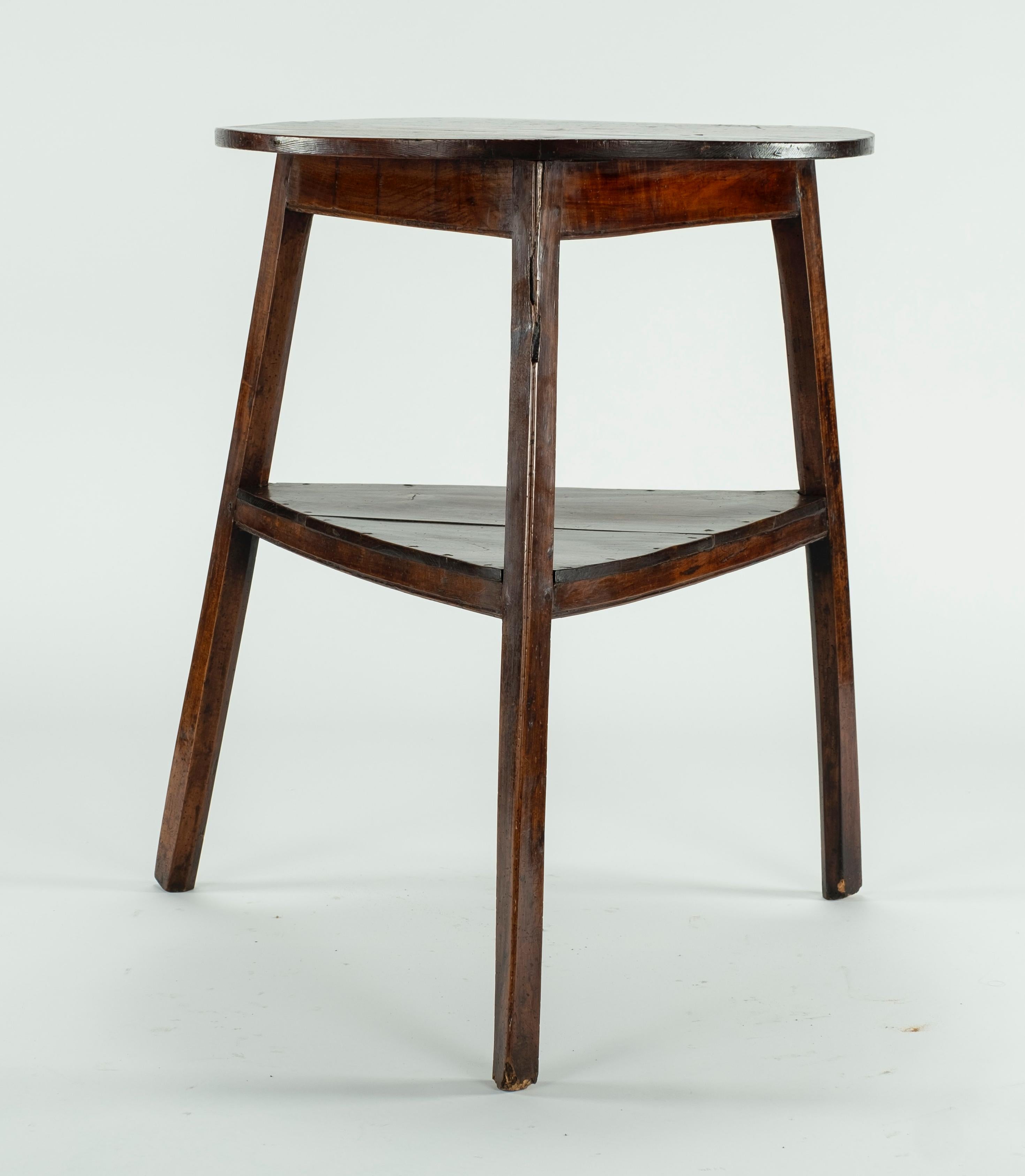 An early 19th century elm and fruitwood high cricket table. The round top on slightly splayed and chamfered legs united by a plank triangular under shelf.