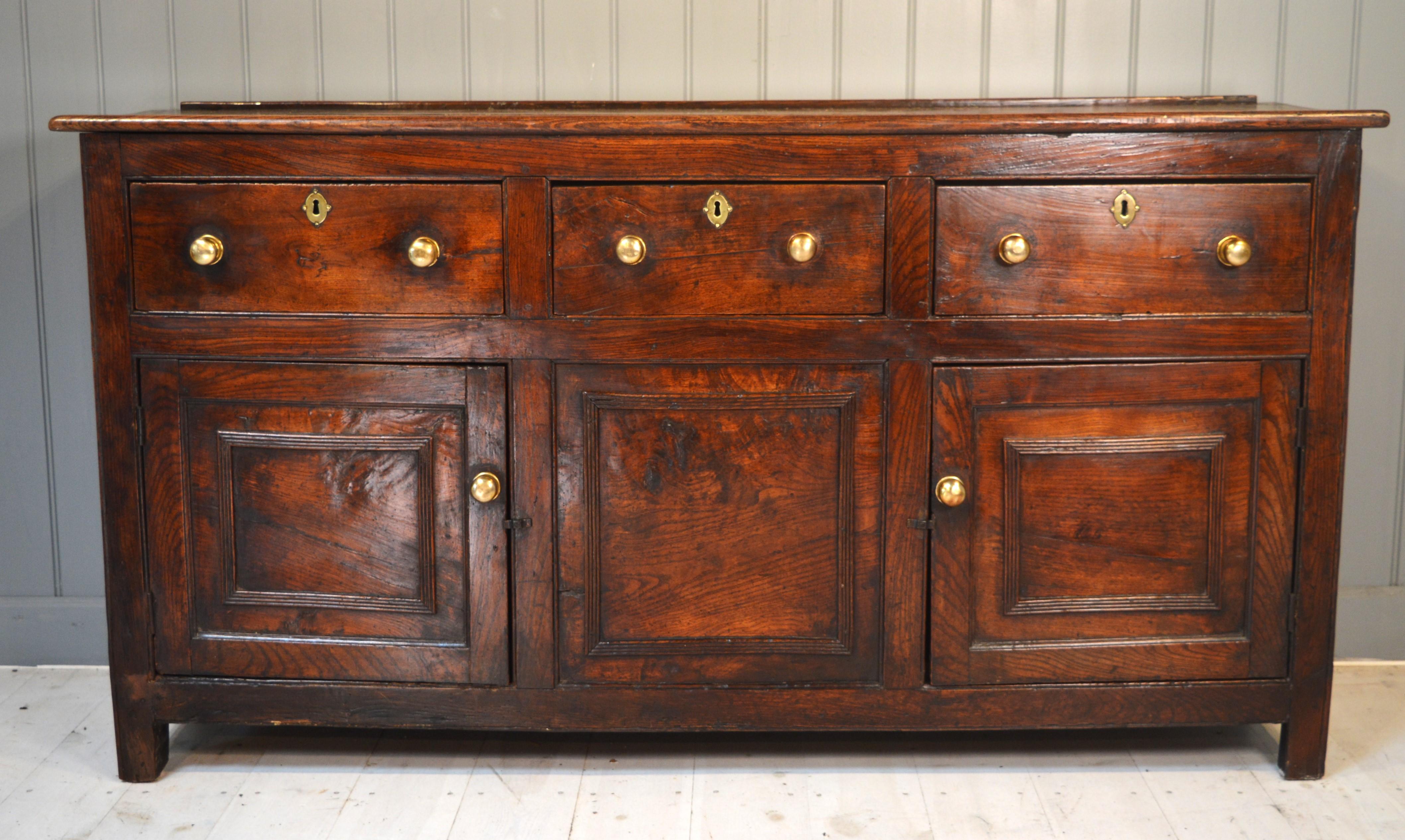 Here we have a warm colored elm dresser base of small proportions with three drawers and two cupboards. The grain is well figured and the patterns are artfully used in the construction. The doors and central panel are decorated with additional