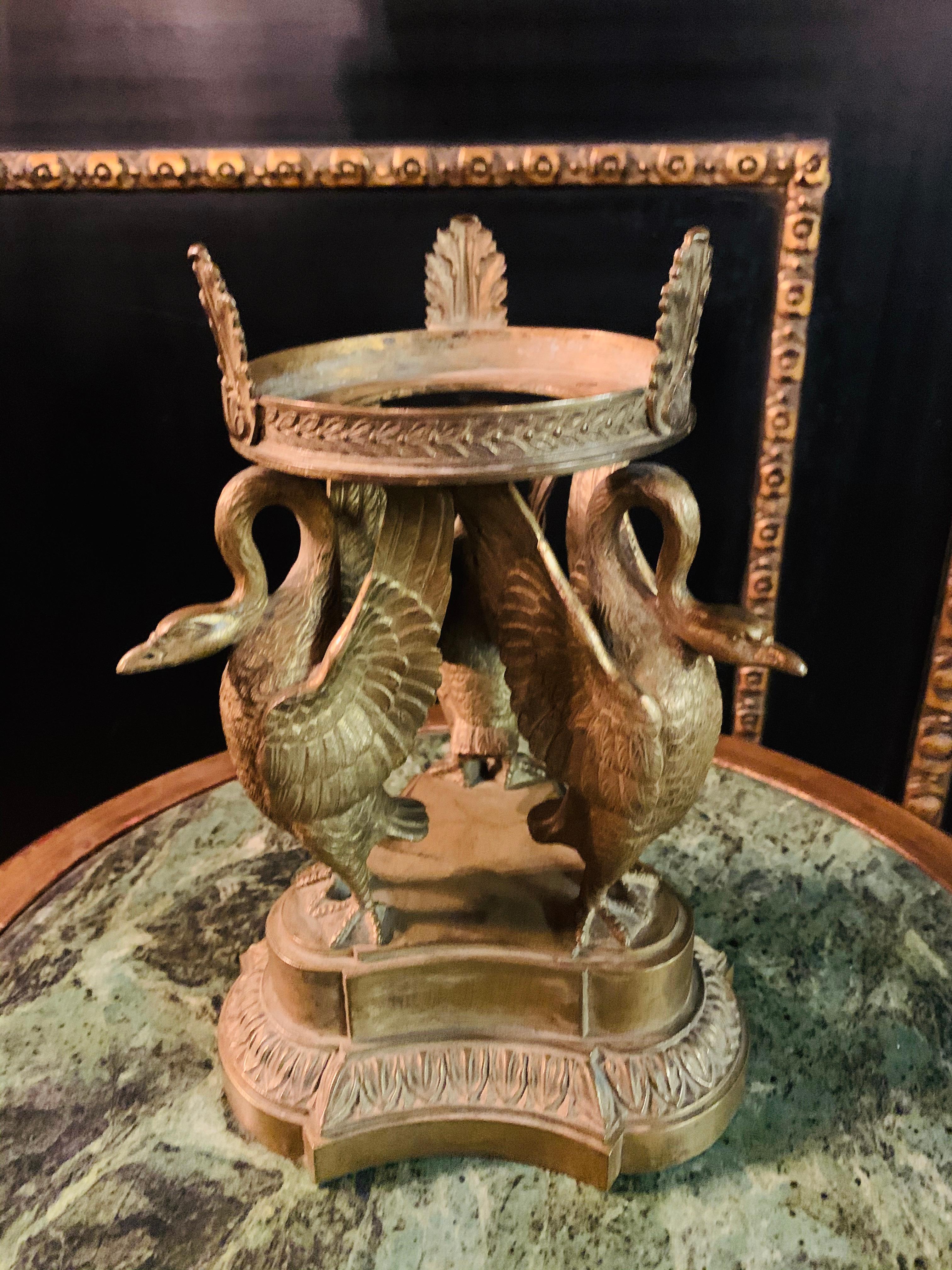 Base of an Empire centerpiece, 19th century bronze with residual gilding. Three-pass, ornamented and profiled postame base. On top of it 3 swans with a wreath on their curved necks and outstretched wings (to accommodate a glass bowl). Gold plating