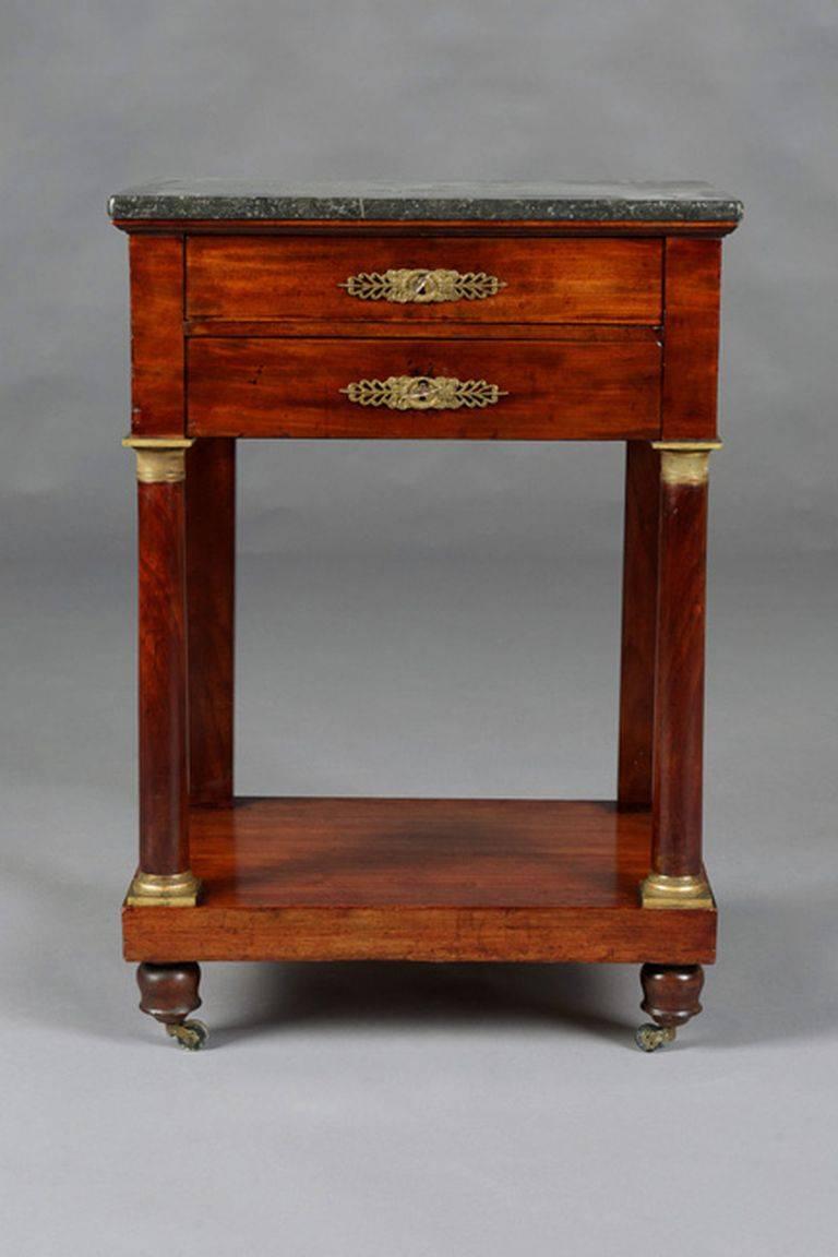 French Empire. Solid mahogany wood. Gilded and chiselled fittings. Two-wise frame base with protruding rectangular marble slab on square columns, joined by an intermediate compartment ending in rollers. Plate with beveled corners. 

(G-54).