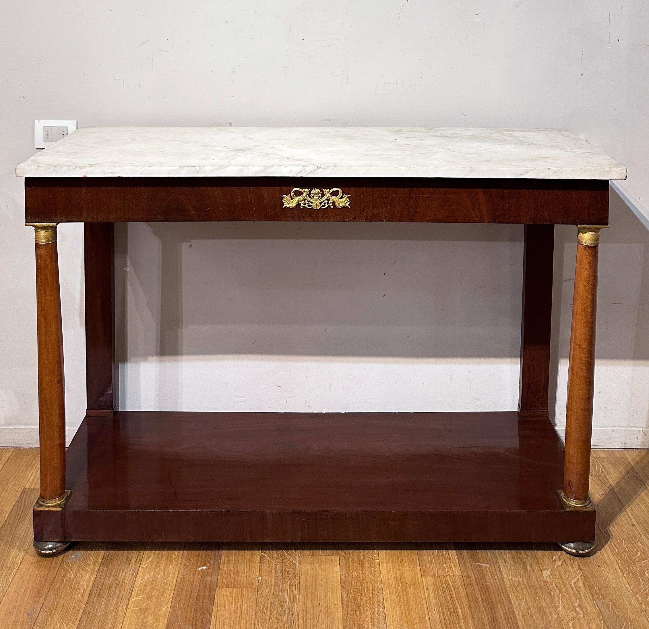 This console from the Empire period (early 19th century) is made with fine mahogany wood paneling, while the columns are made from fir wood. Its structure is embellished with refined finishes and decorations in lost wax, chiseled and gilded bronze,