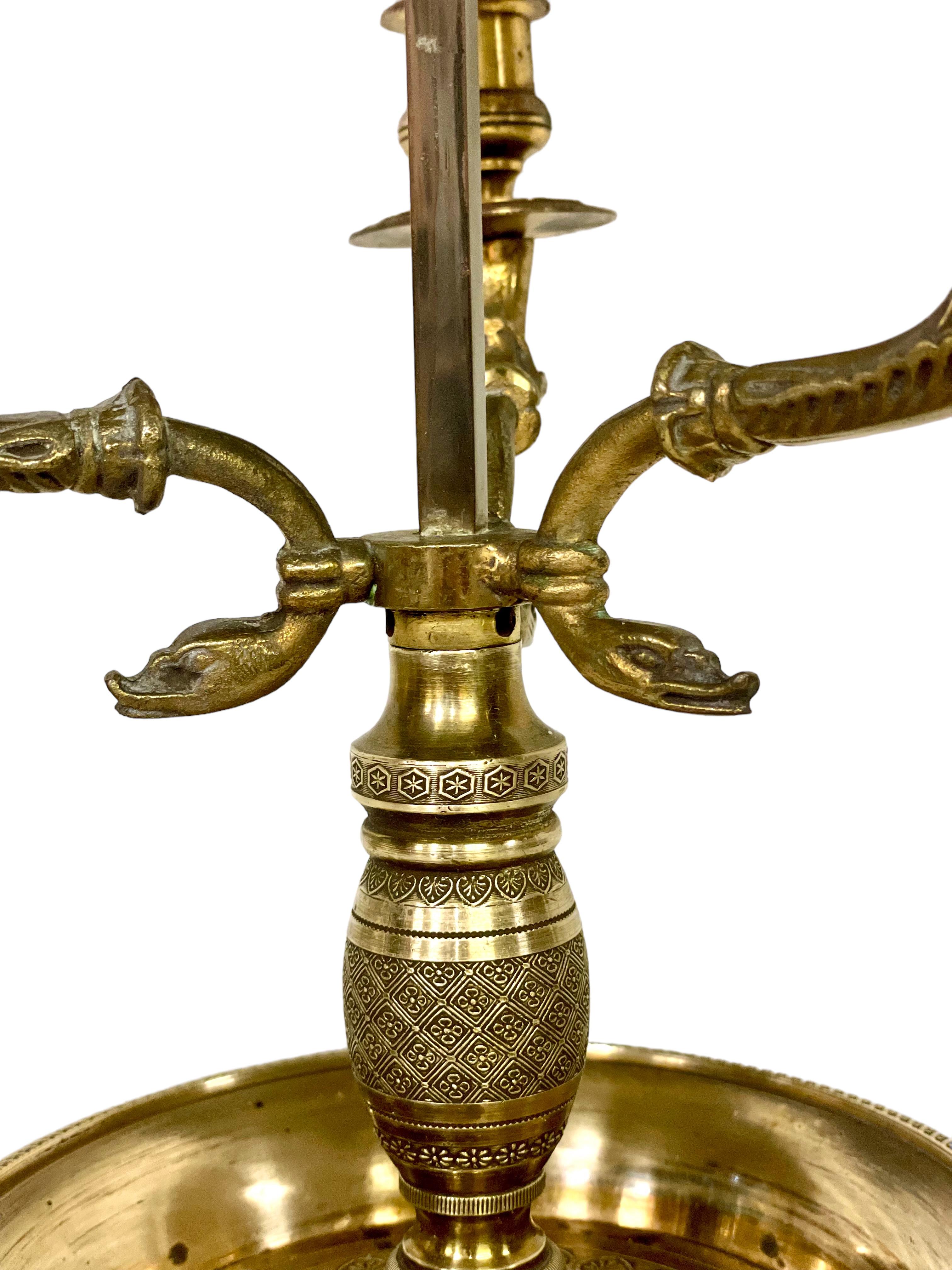 Très élégante lampe de table 'Bouillotte' de style Empire du 19ème siècle en bronze doré, éclairée par trois bras curvilignes en 'tête de cygne' et surmontée d'un abat-jour en métal laqué vert (tole) orné d'une frise de feuilles de laurier. Dotée