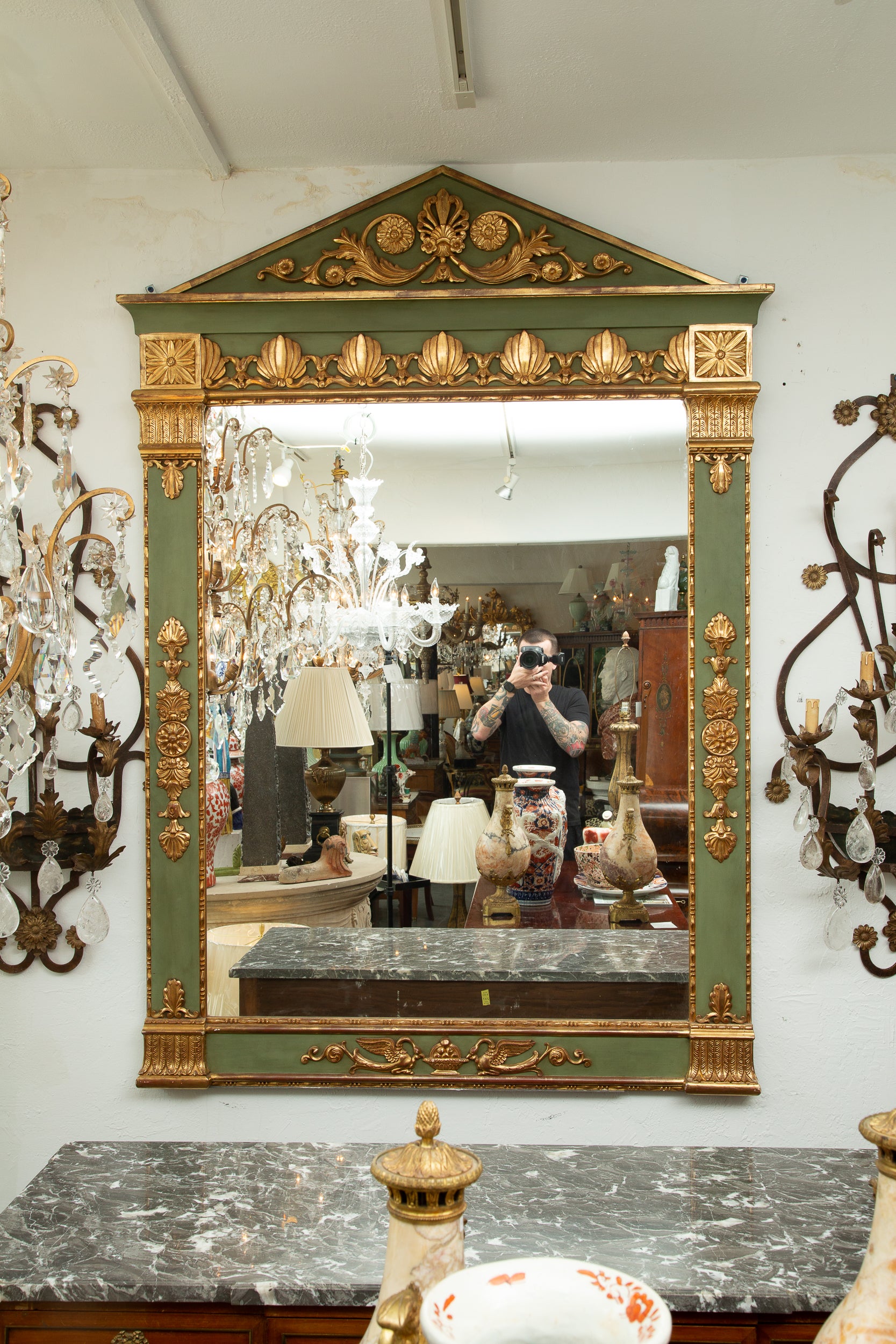 This is a stately green painted and parcel gilt Empire mirror with a triangular cornice over a wide highly decorated frame surrounding a mirror plate, 19th century.