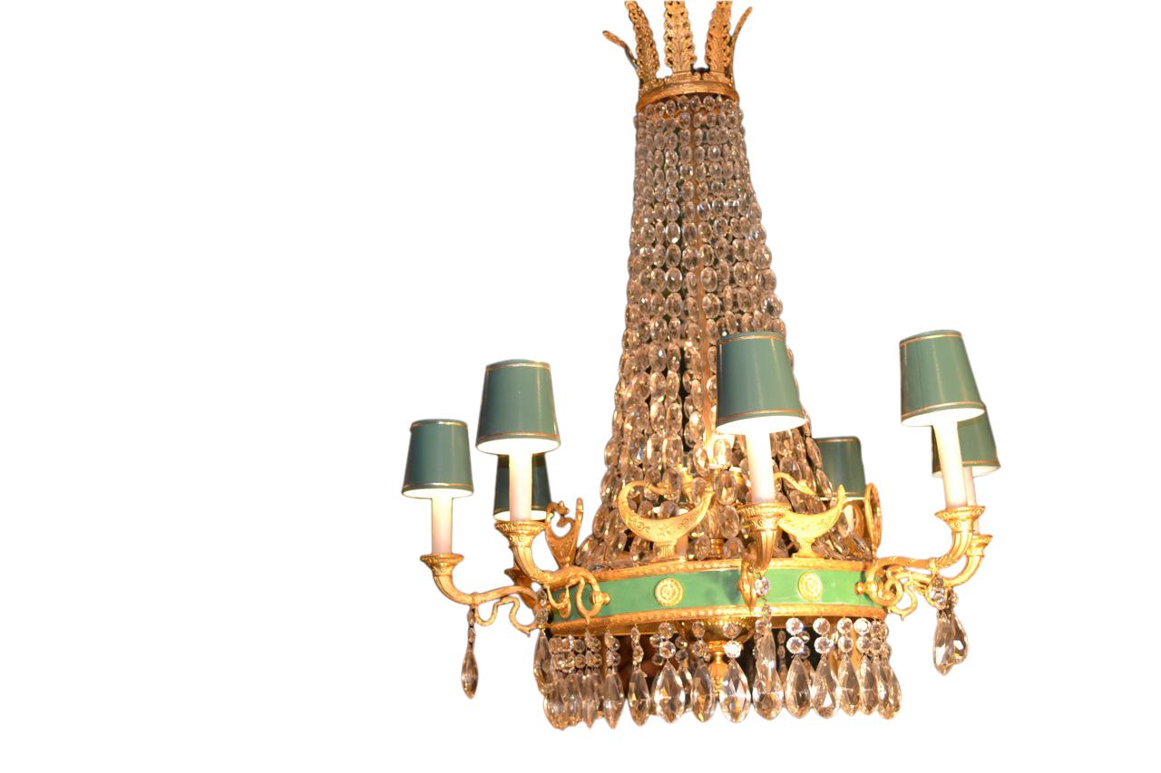 Lampadario in cristallo e bronzo dorato in stile impero francese. La fascia superiore dorata di palmette sostiene stringhe di cristalli tagliati che terminano nell'anello centrale con rosetta dorata, dipinta di verde chiaro, da cui si dipartono