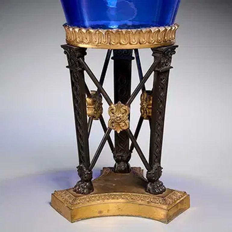 The product is a 19th century Empire style compote featuring gilt bronze accents and cobalt glass. This decorative piece would make a stunning addition to any home décor, adding a touch of vintage charm and sophistication to a living space. Circa