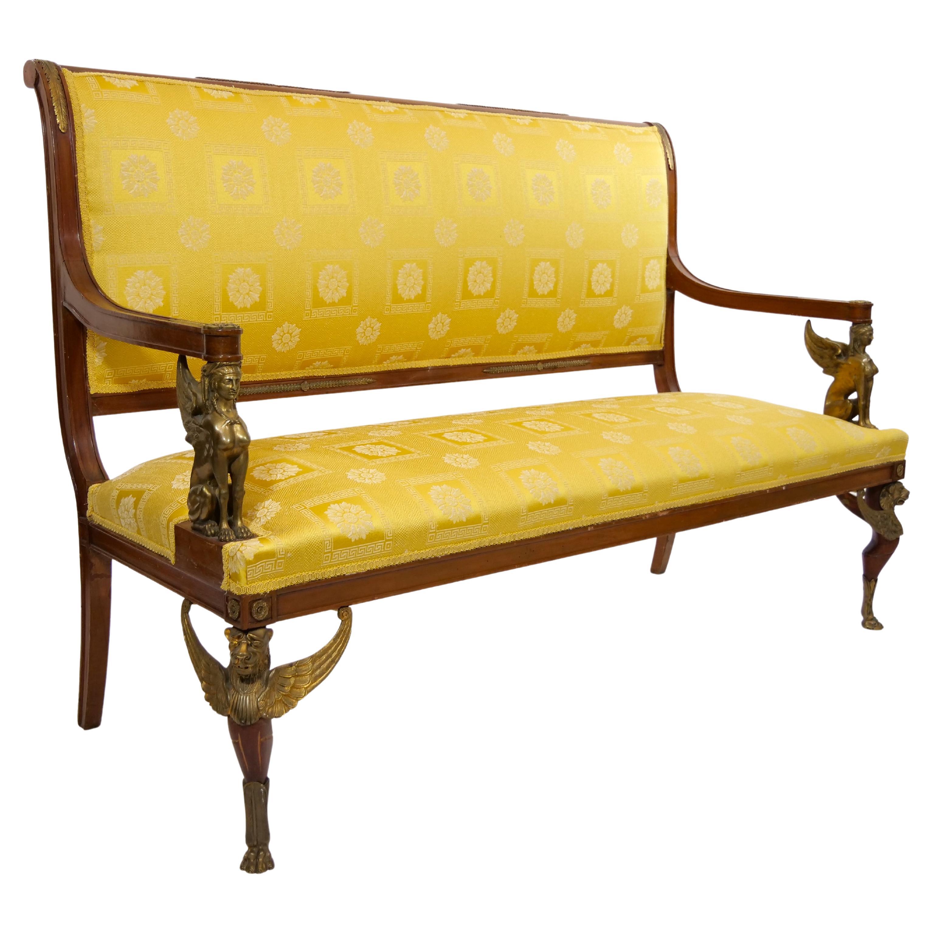19th century French Empire style handcrafted gilt bronze mahogany framed upholstered settee / sofa. The settee features four straight mahogany legs, the front two of which are set on gilt bronze paw feet and Gilt bronze sphinxes serve as arm rests,