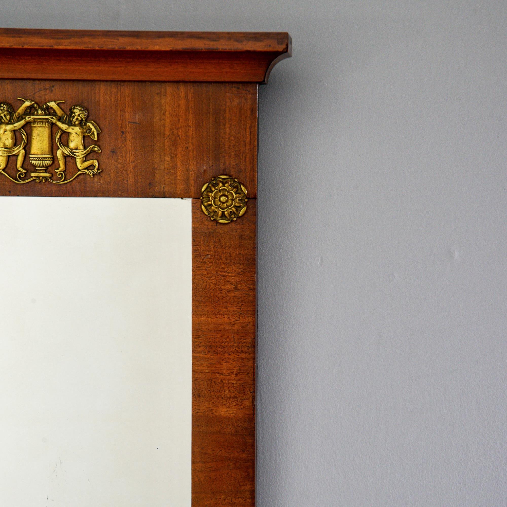 English empire style mirror has a mahogany frame with decorative pediment and Ormolu mounts, circa 1880s. Actual mirror size: 15.75” high x 9” wide.