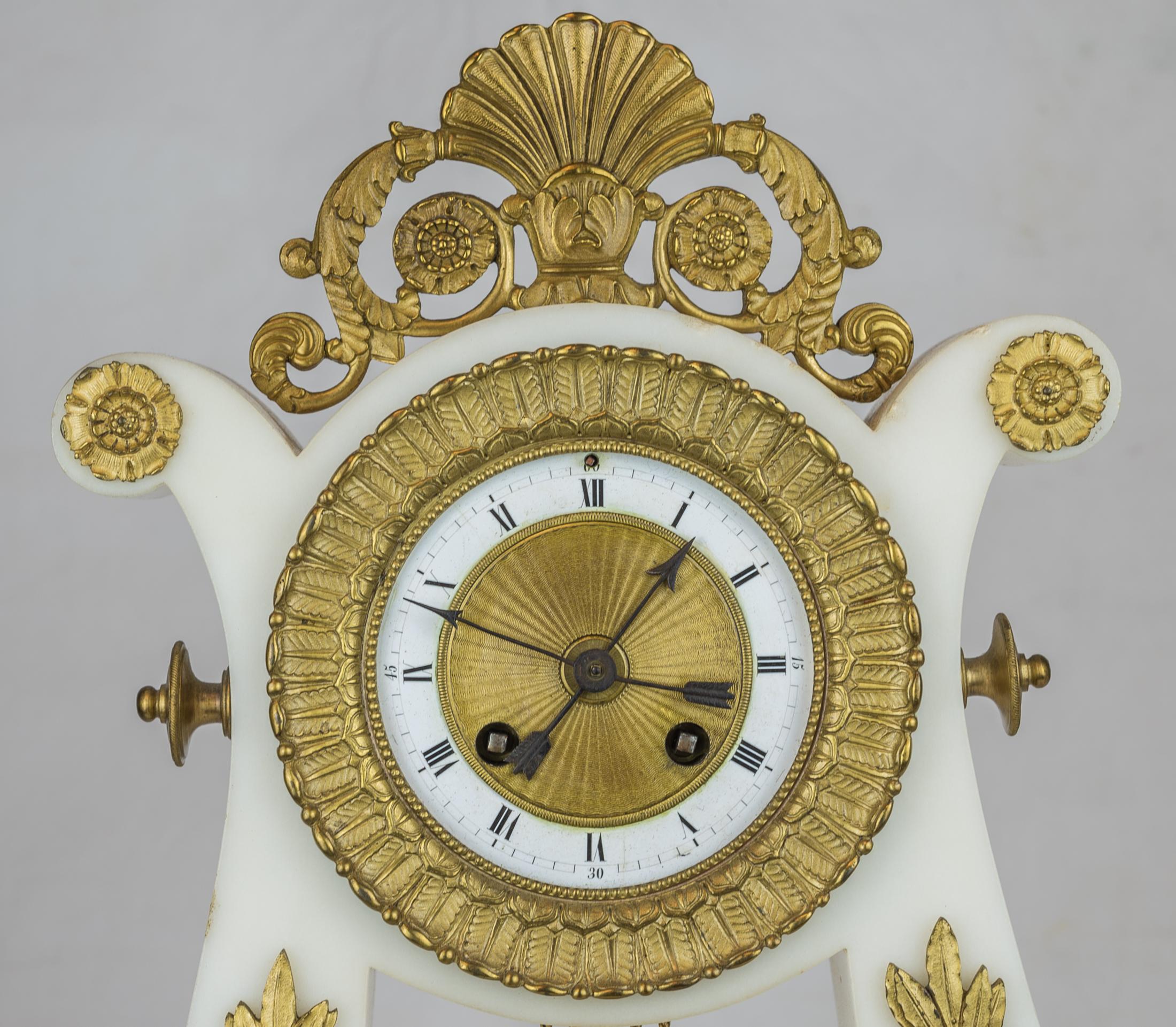 A Luxurious 19th century Empire style ormolu and white marble lyre clock garniture.
Known as a lyre clock for its graceful shape, this elegant piece is crafted with white marble and luxurious ormolu acanthus leaf and scroll in the Empire-style.