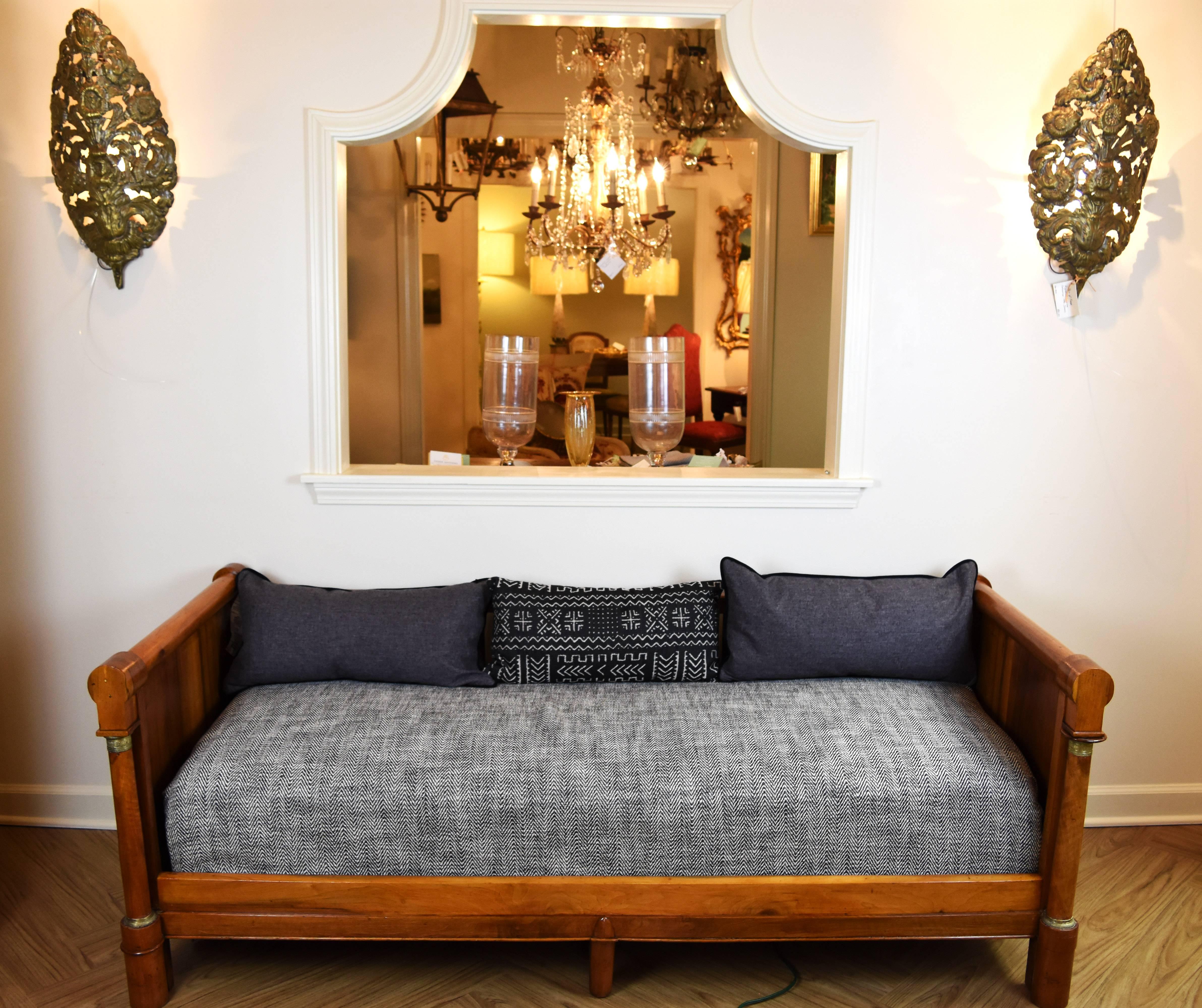 This Empire style daybed features a beautiful walnut frame with carved column legs. Each column has bronze ornamentation at the top and bottom. 
 The daybed comes with the seat cushion shown but not the seat back pillows.