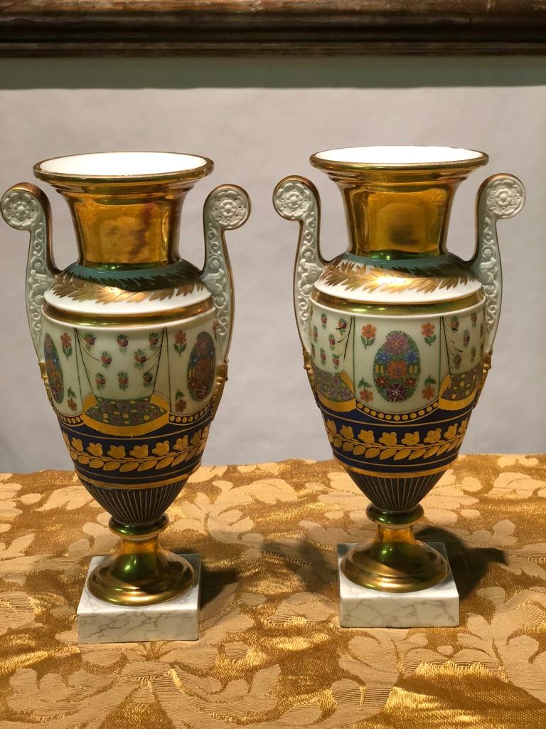 Important pair of Empire ceramic vases with polychrome decorations with floral and gold motifs. Handles shaped with Classic motifs. The vases resting on a pedestal whose base is square and the upper edge flares into a molded rim and is provided on