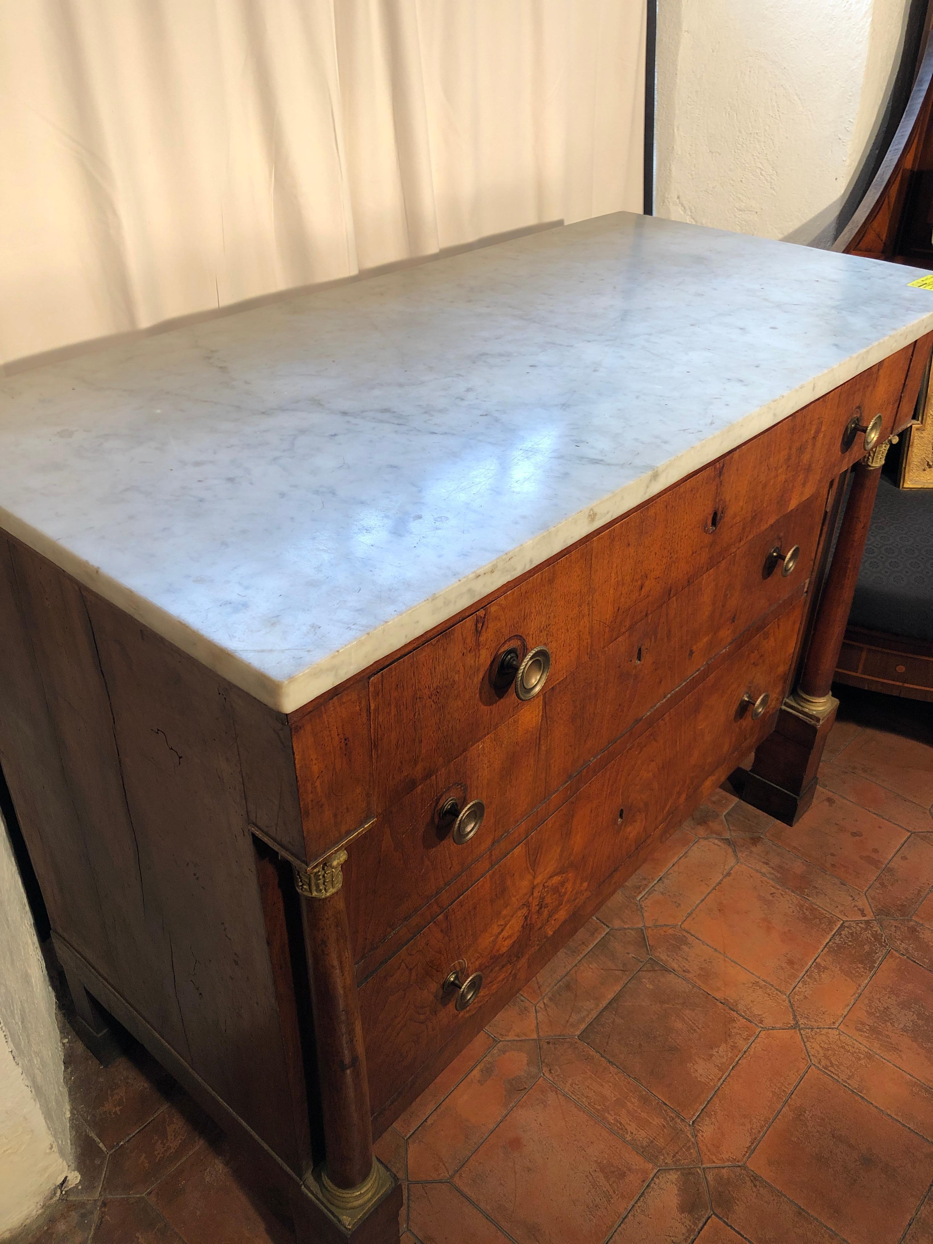 Chest of drawers empire of Tuscany origin, probably city of Lucca, in walnut wood with full columns always in walnut, the capitals are in gilded wood. Feet in plinth and contemporary marble in white Carrara of the time. Bring back the initials on