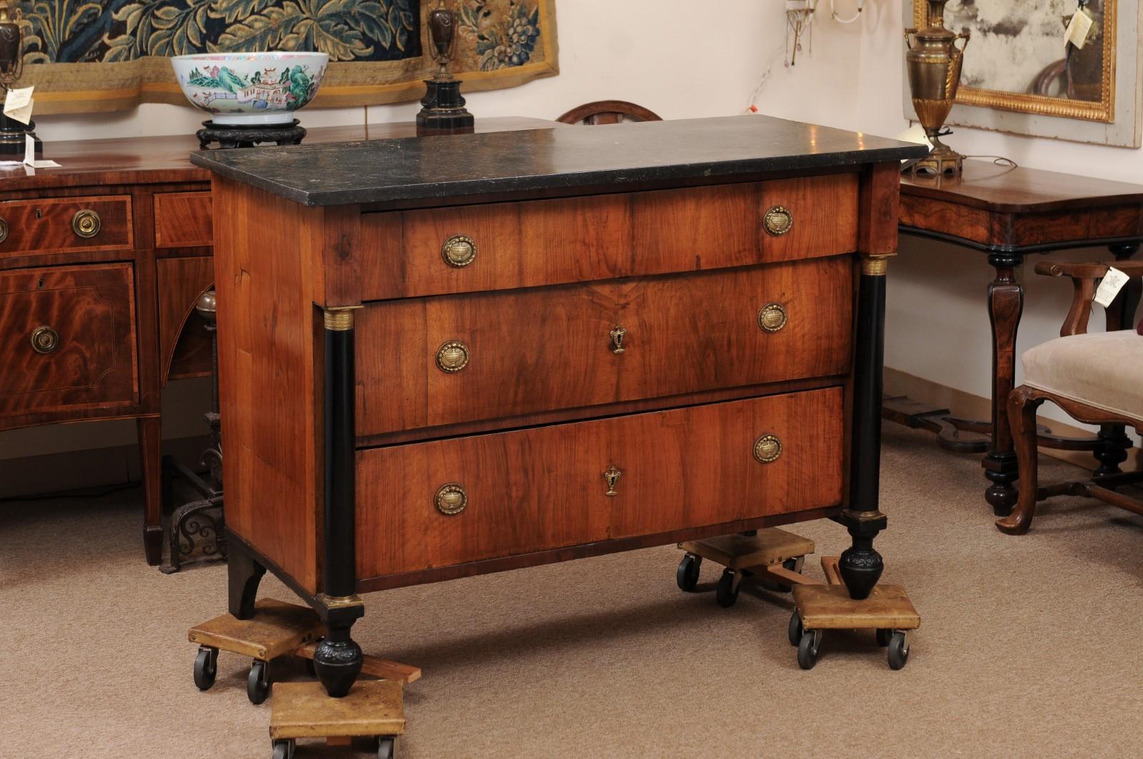 Empire Period commode with black marble top, light walnut patina, three drawers, flanking ebonized columns with gilt mounts and all resting on turned feet, 19th century Continental Europe.