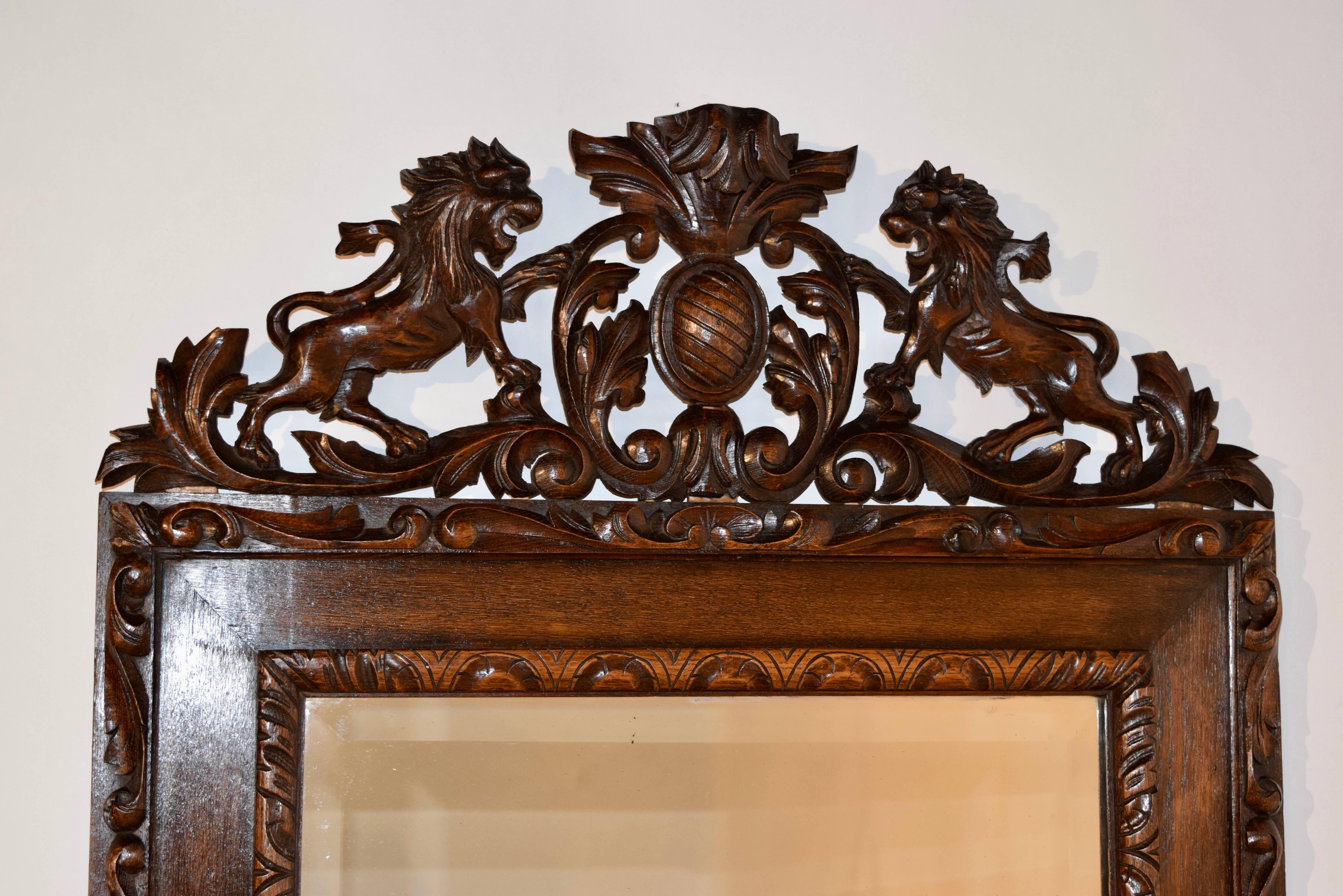 19th century English mirror with lovely hand-carved borders around the inner and outer edges of the frame and a hand-carved armorial on the top of the mirror depicting two lions flanking a plaque.