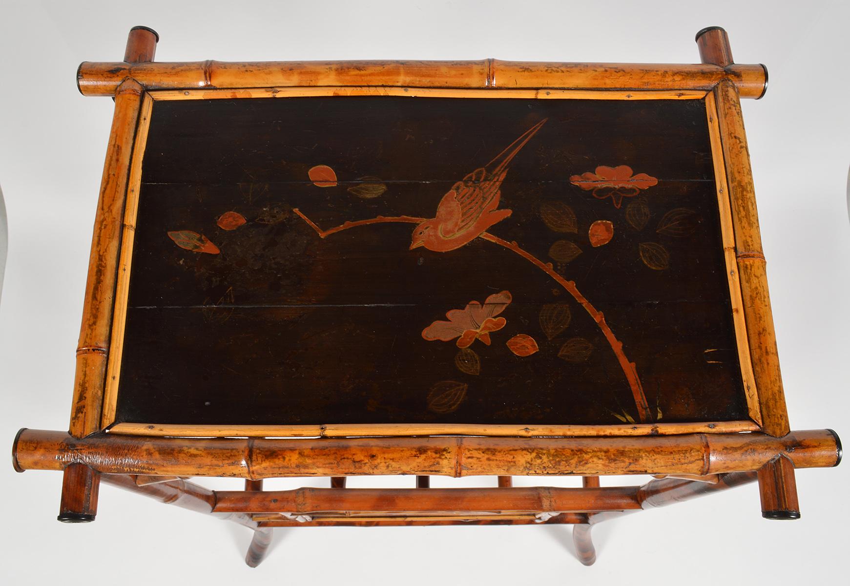 Dieser ungewöhnliche englische Bambustisch aus dem 19. Jahrhundert dient sowohl als Tisch als auch als Zeitschriftenständer. Auf der mit Japanglasur lackierten Oberseite ist ein Vogel in einem Garten abgebildet:: und die beiden Tafeln weisen ein