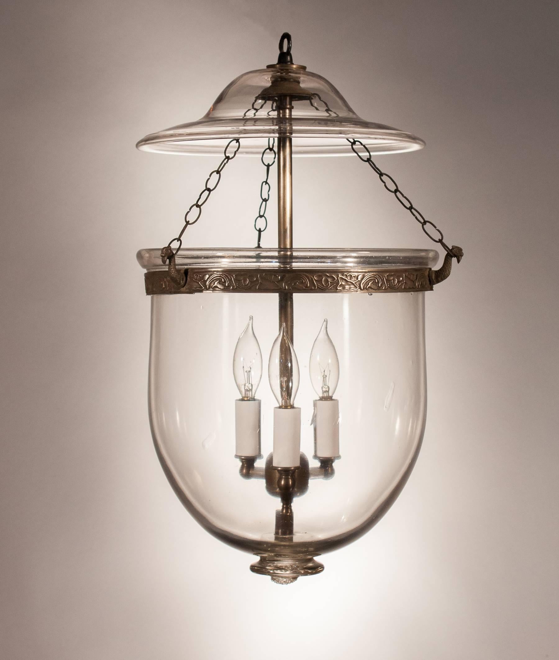 Classic handblown clear glass bell jar lantern from England, circa 1870. This shapely hall lantern has its original smoke bell at top and a well-proportioned glass pontil at bottom. The brass band, which has an embossed vine motif, has been replaced