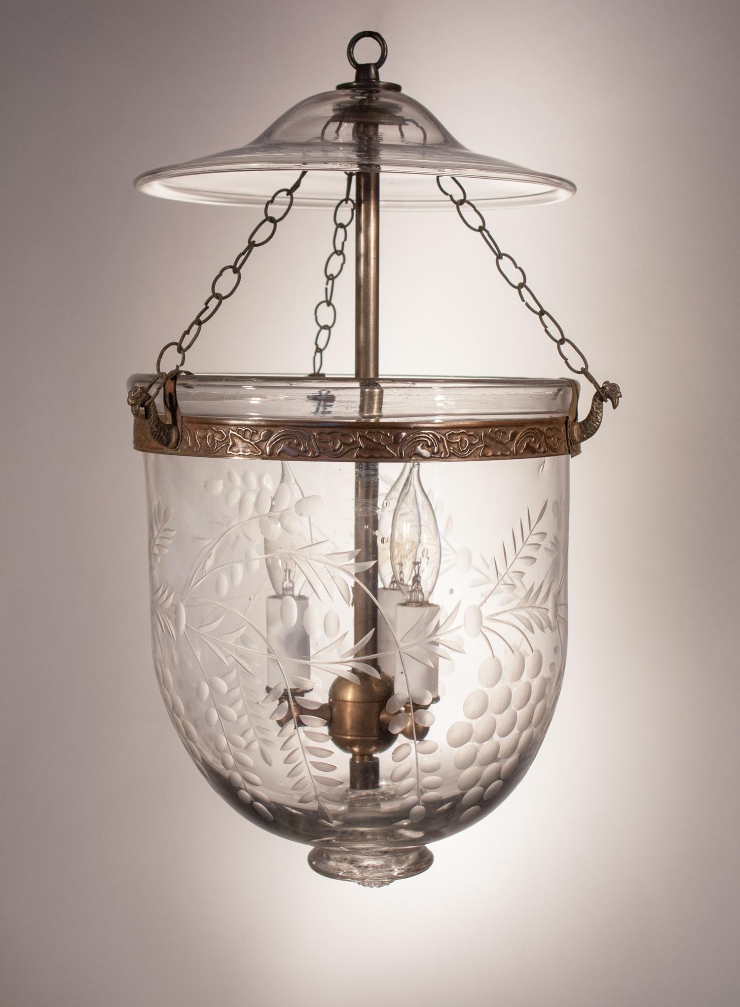 An antique bell jar lantern with etched grape and vine motif. This charming circa 1890 lantern has its original smoke bell and chains. The embossed brass band, which has a meandering vine design, has been replaced to ensure the pendant's security.