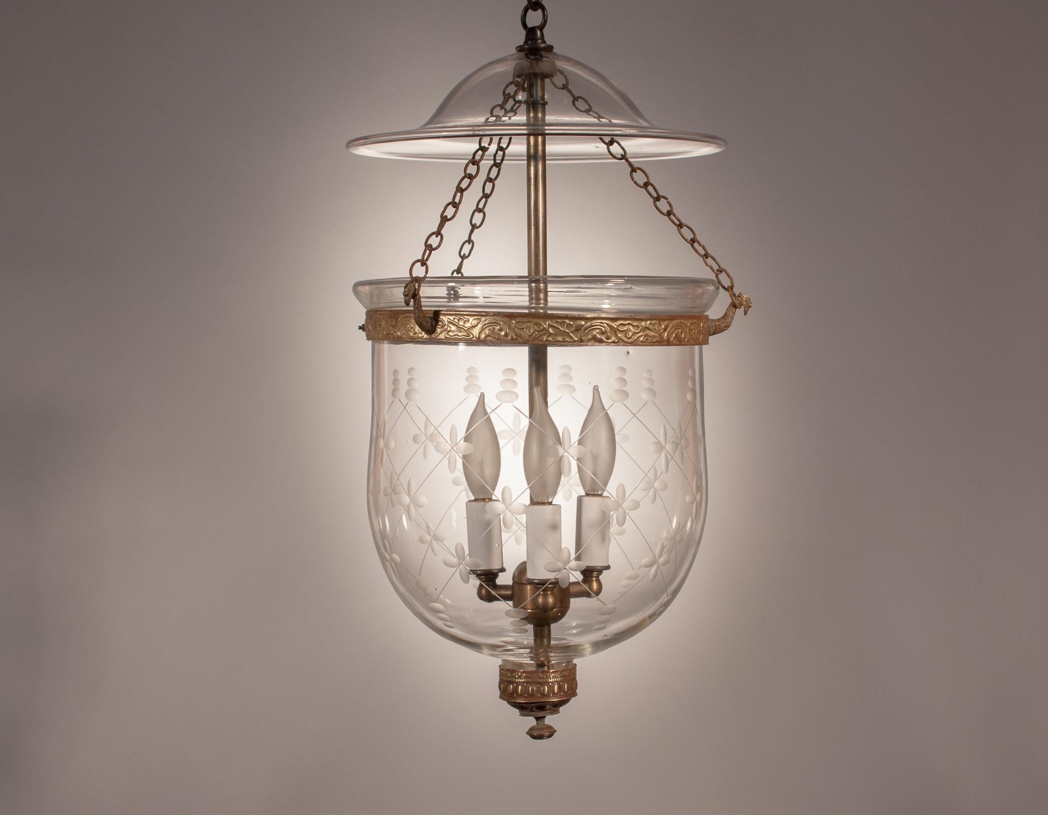 A fine quality handblown glass bell jar lantern having an etched trellis pattern that complements the full form of this shapely hall lantern. The lantern's embellished brass finial and embossed brass band have a rich gold tone. The band and chain