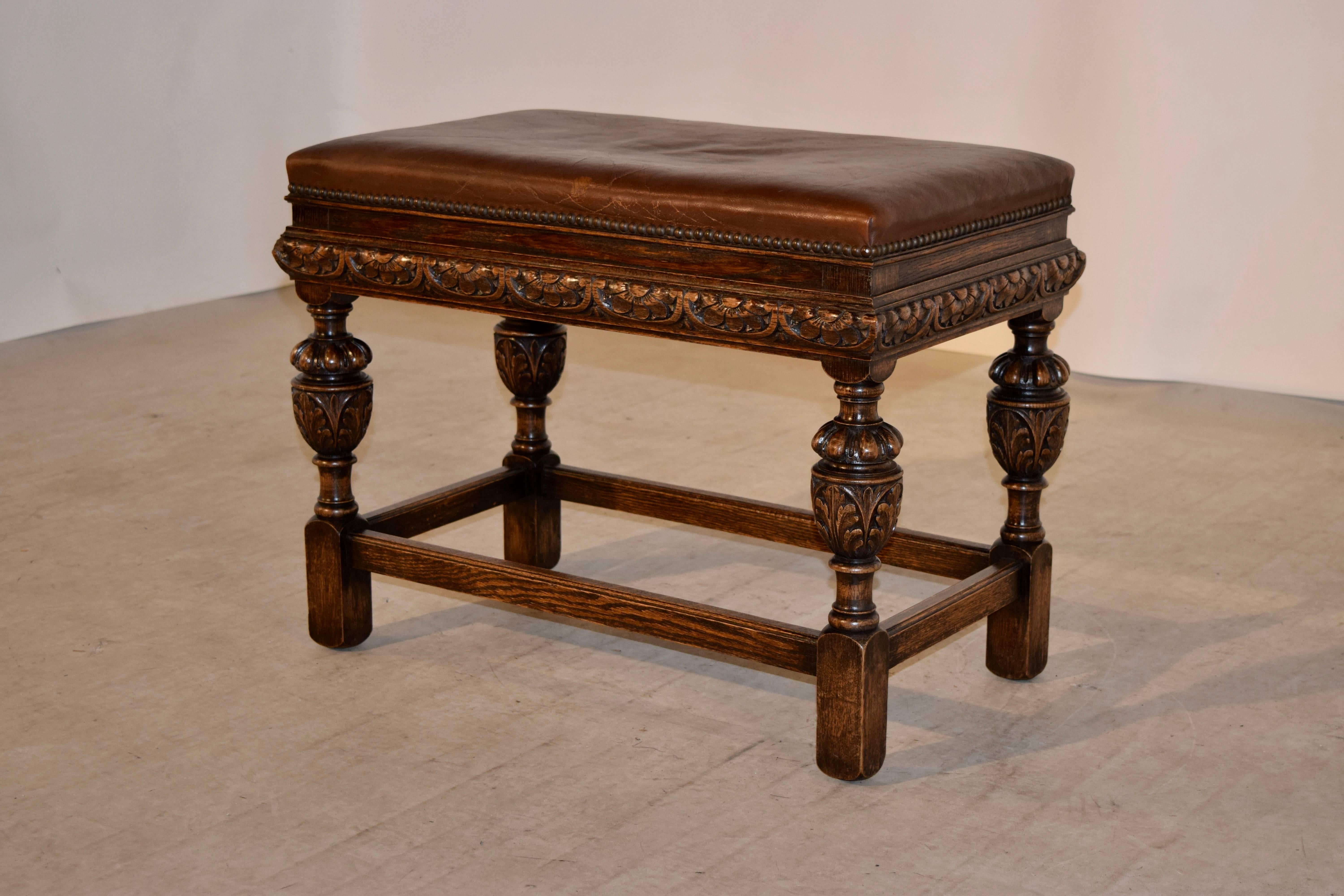 19th century oak bench from England with an upholstered leather top, decorated with brass nails, following down to a hand-turned and carved decorated frame and legs, joined by simple stretchers.