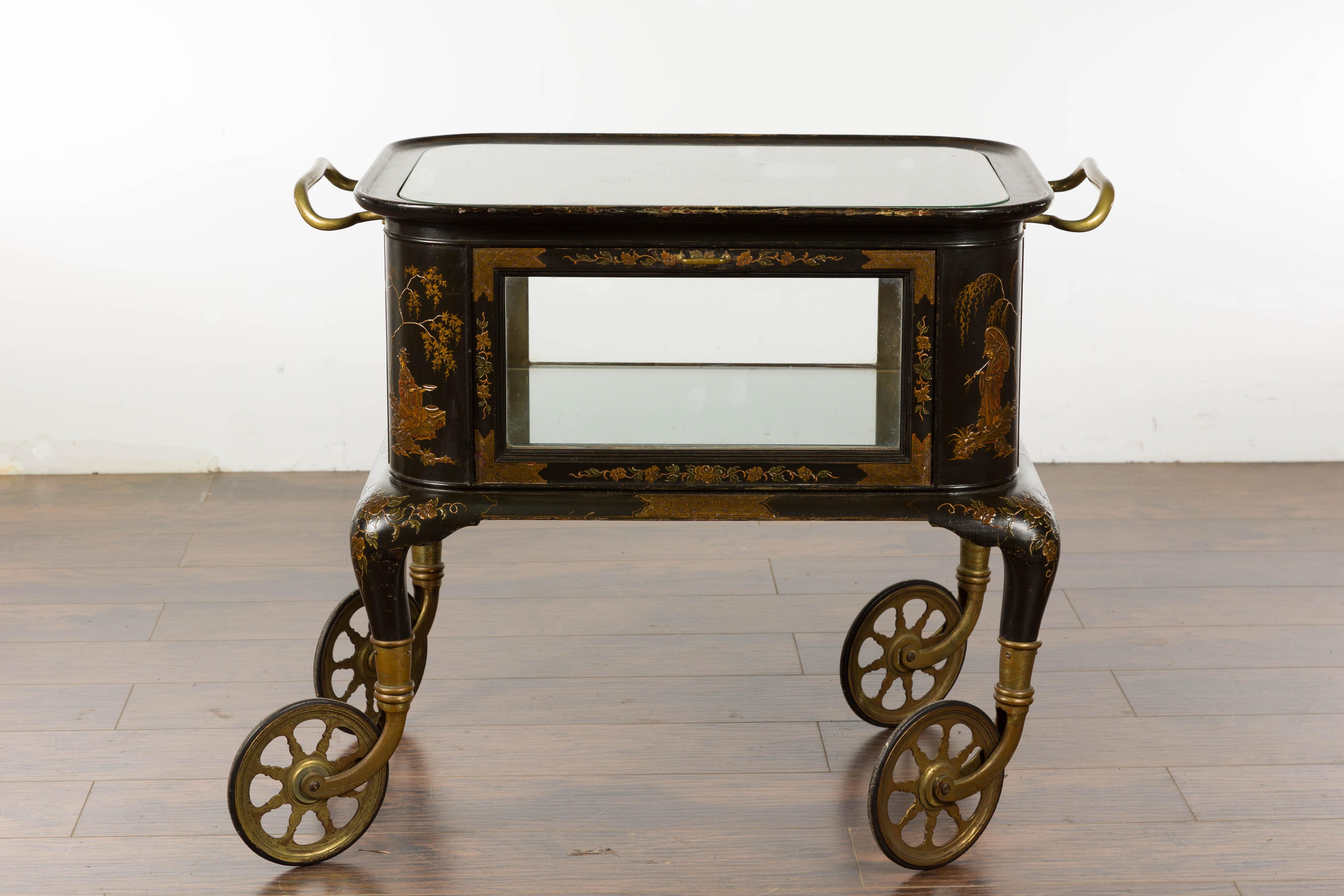 An English black and gold japanned bar cart from the 19th century with Chinoiserie décor depicting figures in landscapes, glass top and sides, on brass wheels. Impress your guests with the sophistication of this 19th-century English black and gold