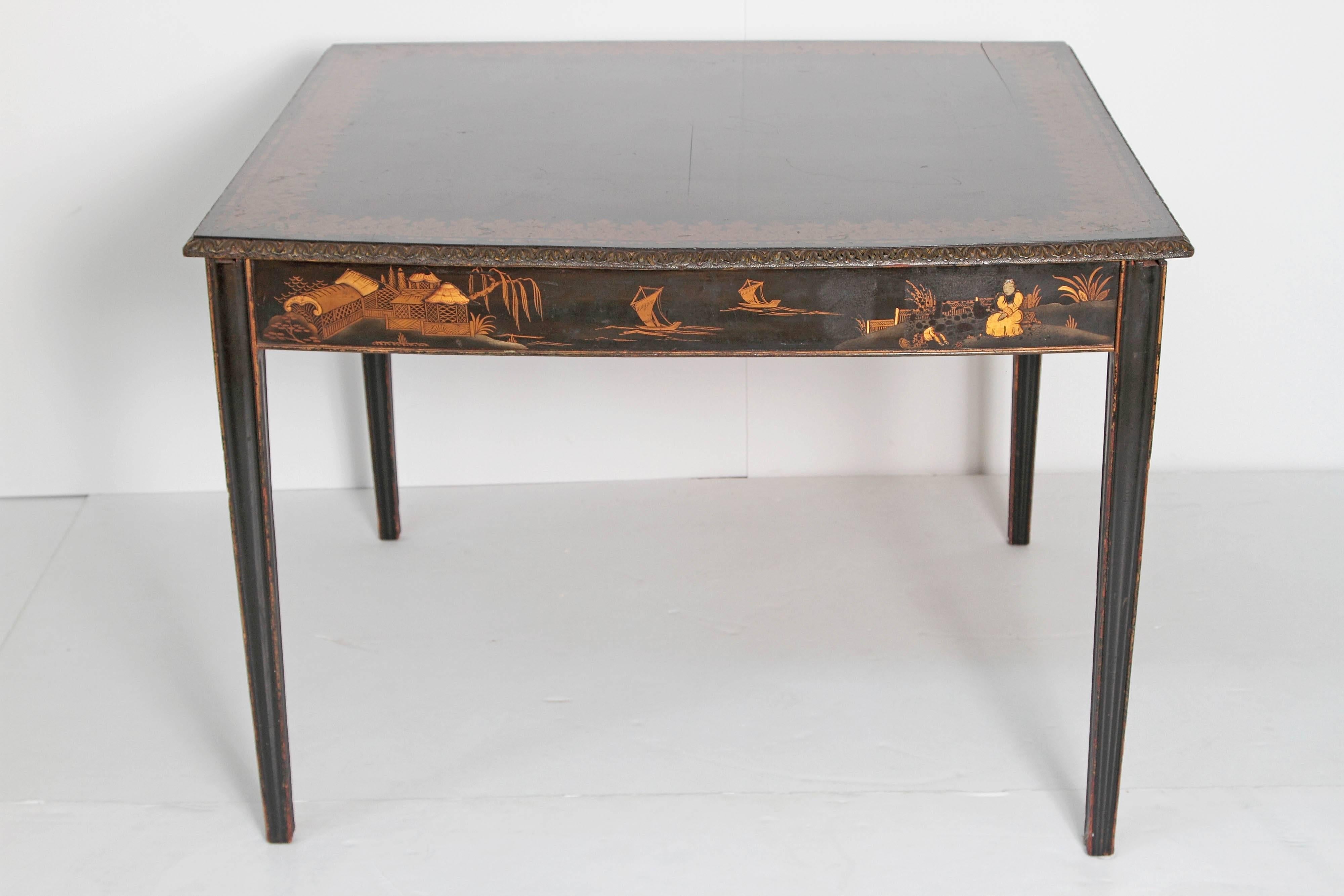 A square black lacquer chinoiserie card / games table with slightly bowed sides. Top with carved edge and overall painted gold acanthus leaf border. Each apron has gold painted scenes of daily life including house, people, boats and birds. Tapered