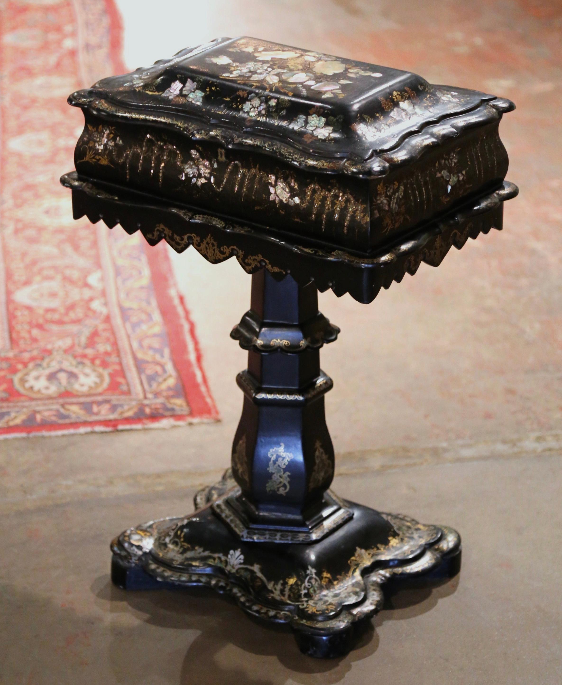 This elegant, hand painted antique sewing table was created in England circa 1880. Standing on a rectangular base with scalloped edges over a thick carved central stem, the cabinet built of 