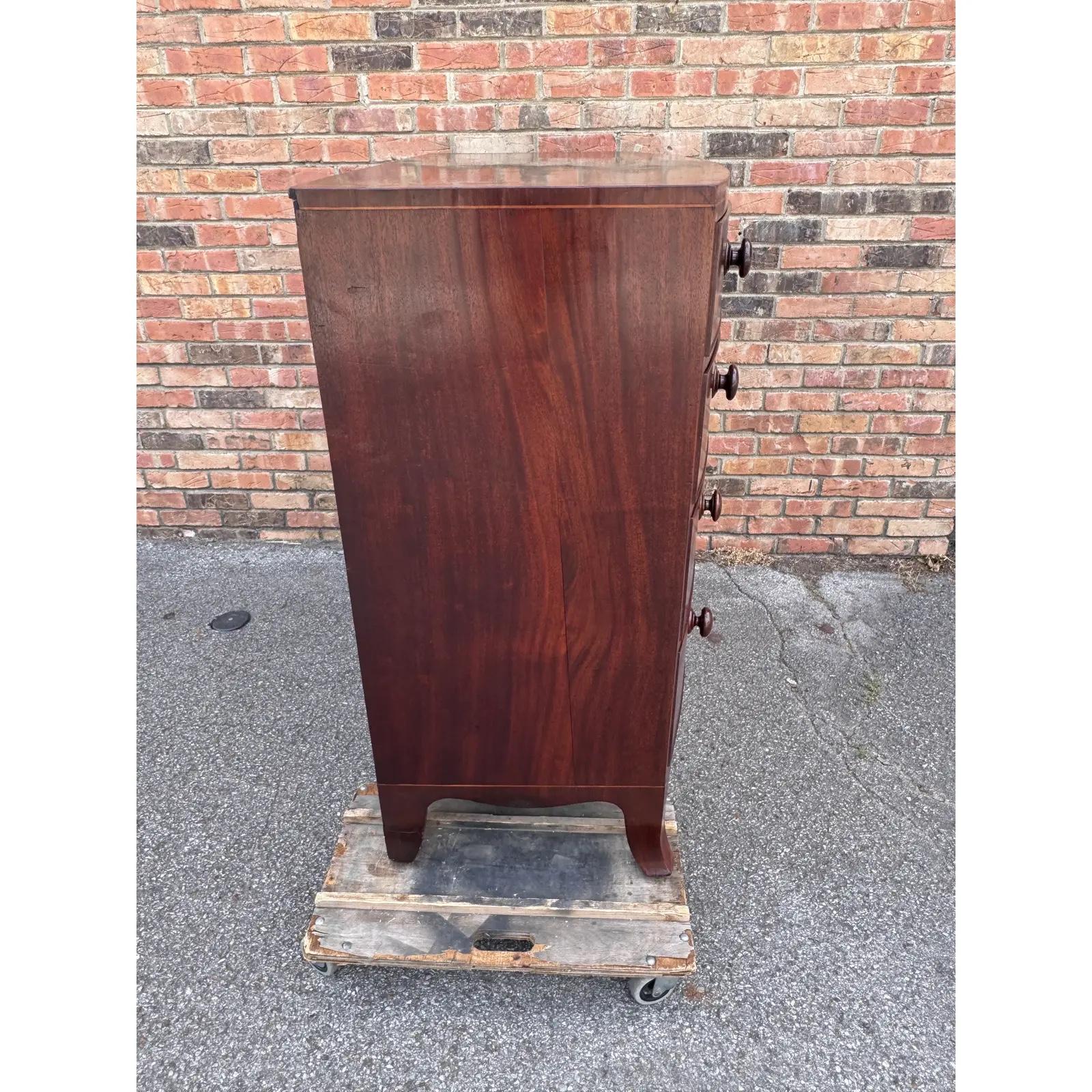 Diese englische Bow Front Chest of Drawers aus dem 19. Jahrhundert ist ein wunderschön gestaltetes Möbelstück mit geschmackvoll verjüngten Beinen, fein geformten Schubladenfronten und hübschen Intarsienverzierungen. Es zeichnet sich durch