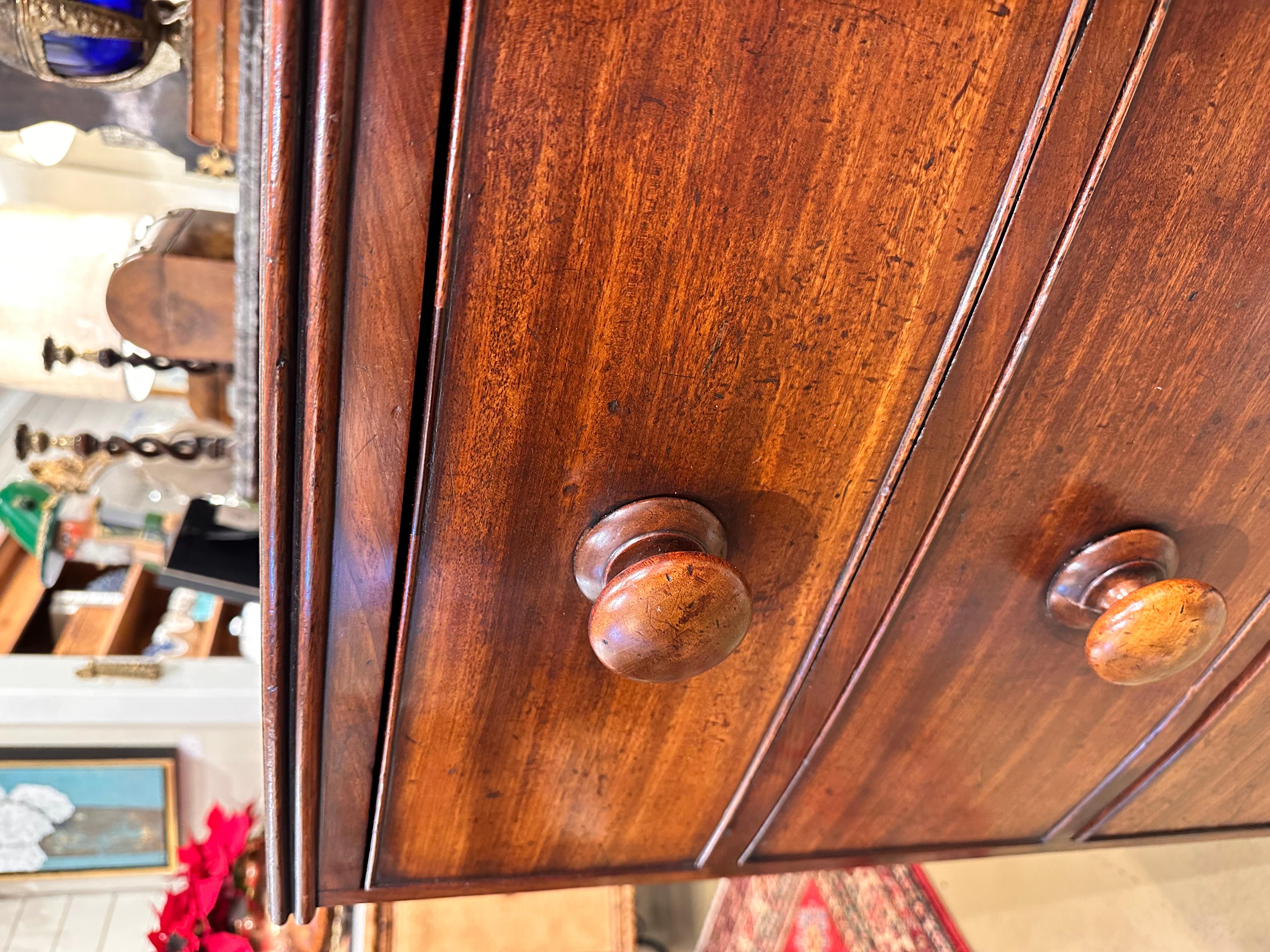 This is a beautiful little English bowfront chest! This piece has a very simple design without lacking elegance. The wood is dark and glossy, with beautiful patina and natural detail showing in the top and front. The wooden knobs maintain the simple