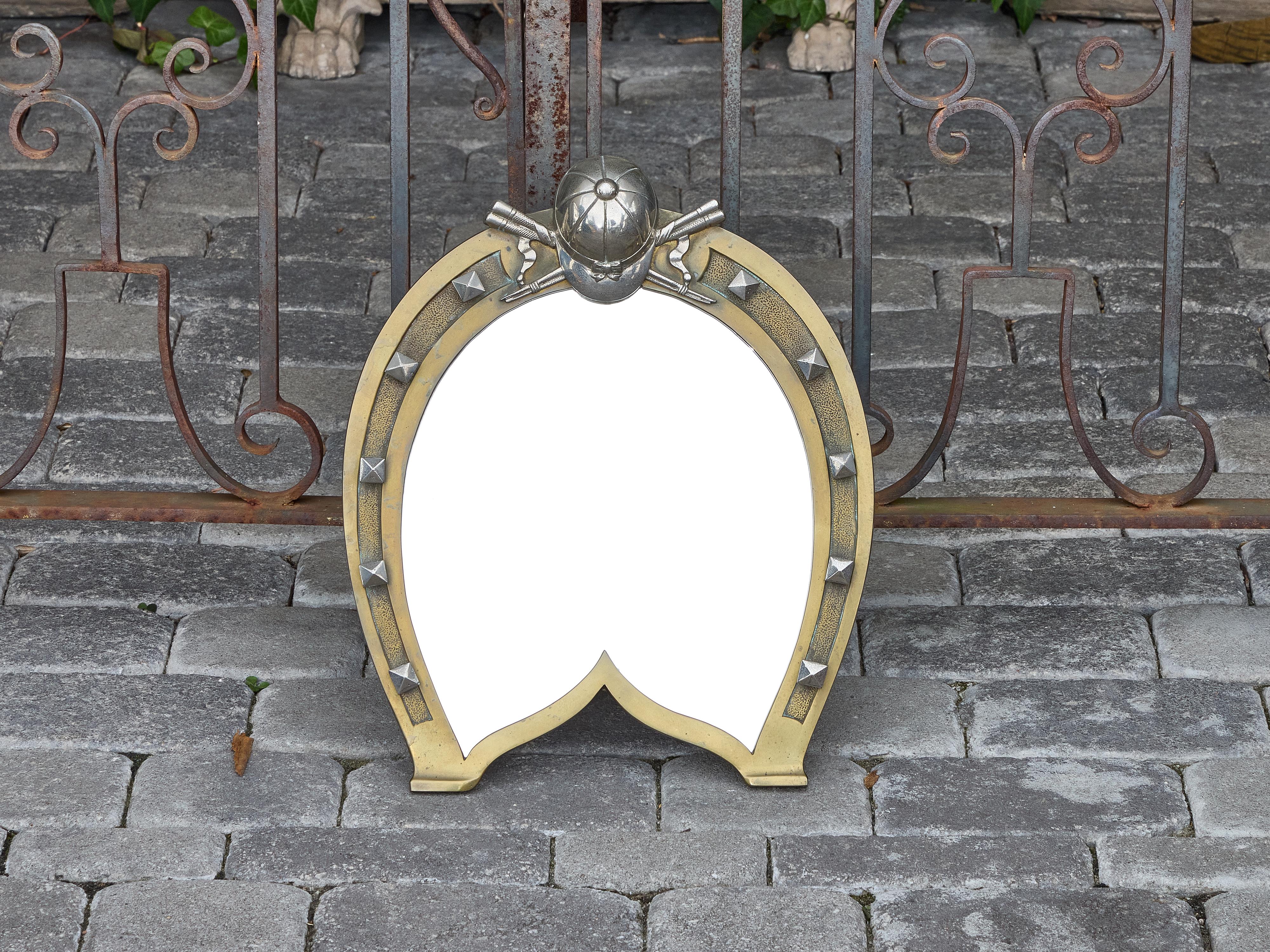 Miroir de table anglais du XIXe siècle, à la fois fantaisiste et finement ouvragé, coulé en laiton en forme de fer à cheval stylisé, complété par des têtes de clous cloutées et surmonté d'un arrangement sculptural de pistolets croisés, d'une