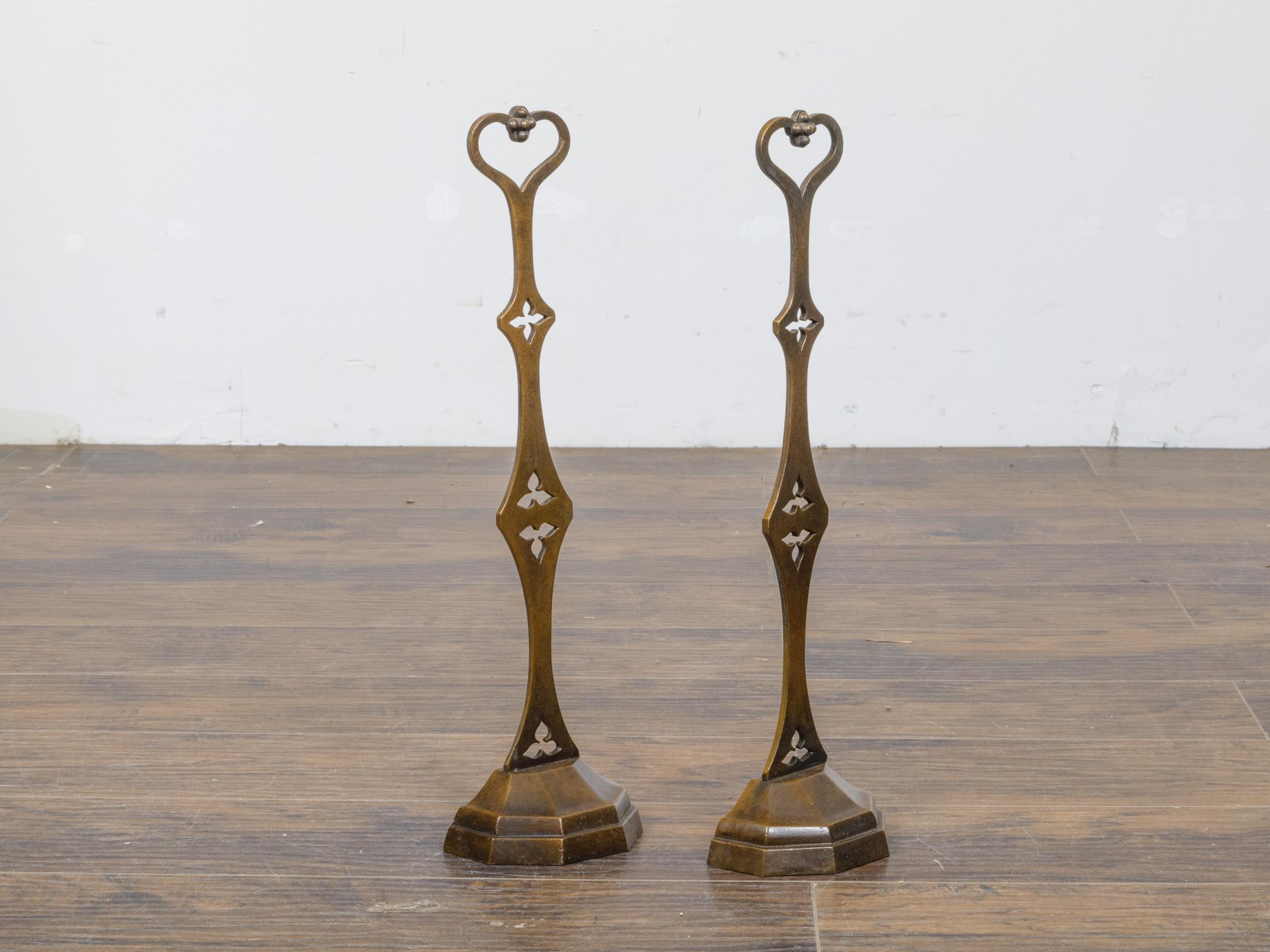 These elegant 19th-century English bronze andirons are a striking blend of functional design and decorative artistry. Their slender silhouettes are adorned with Gothic-style trefoil and quatrefoil cutouts, lending them an architectural charm. The