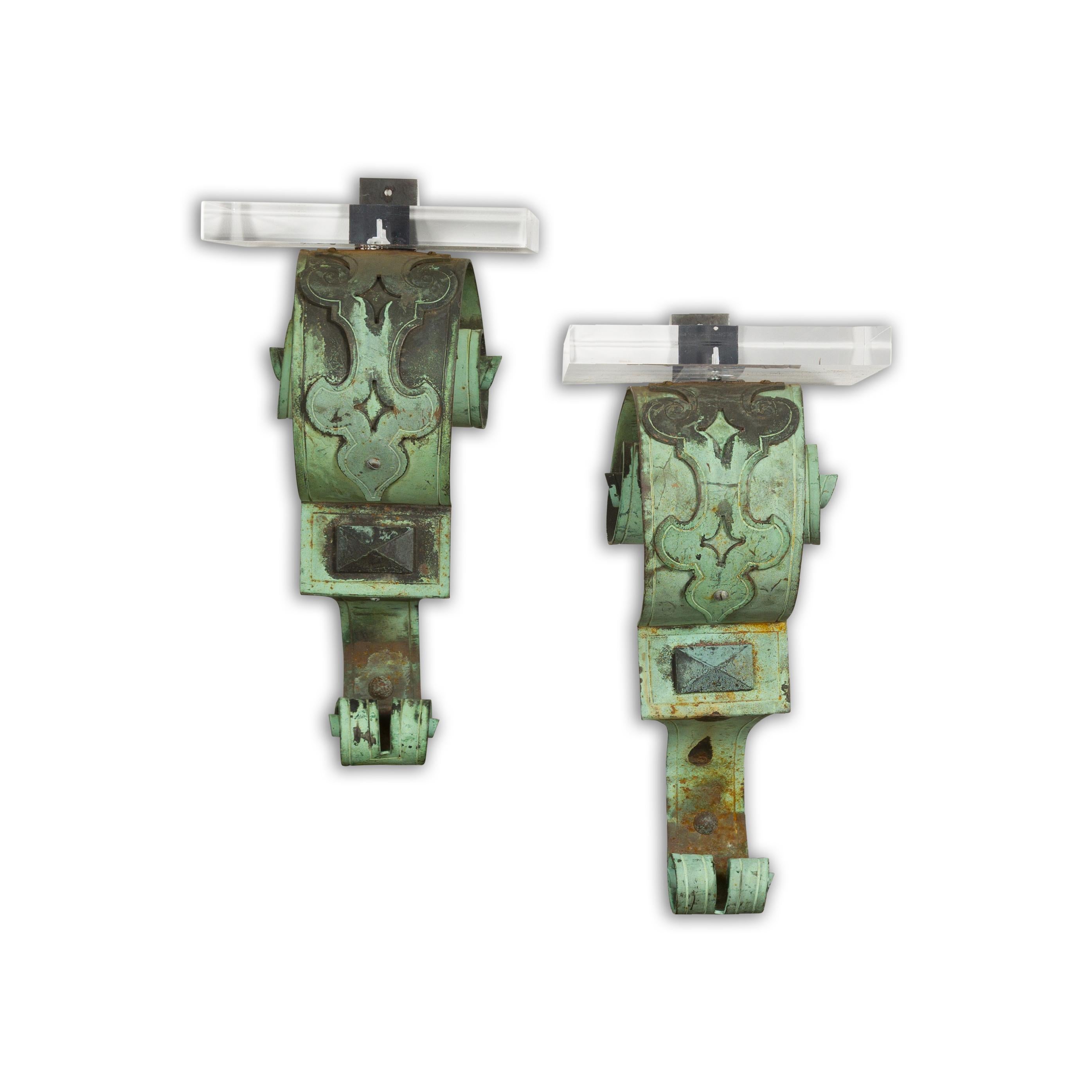 A pair of English bronze wall brackets from the 19th century with lucite tops, scrolling motifs and verdigris patina. Elegantly crafted, this pair of 19th-century English bronze wall brackets exudes a classic charm that transcends time. Adorned with