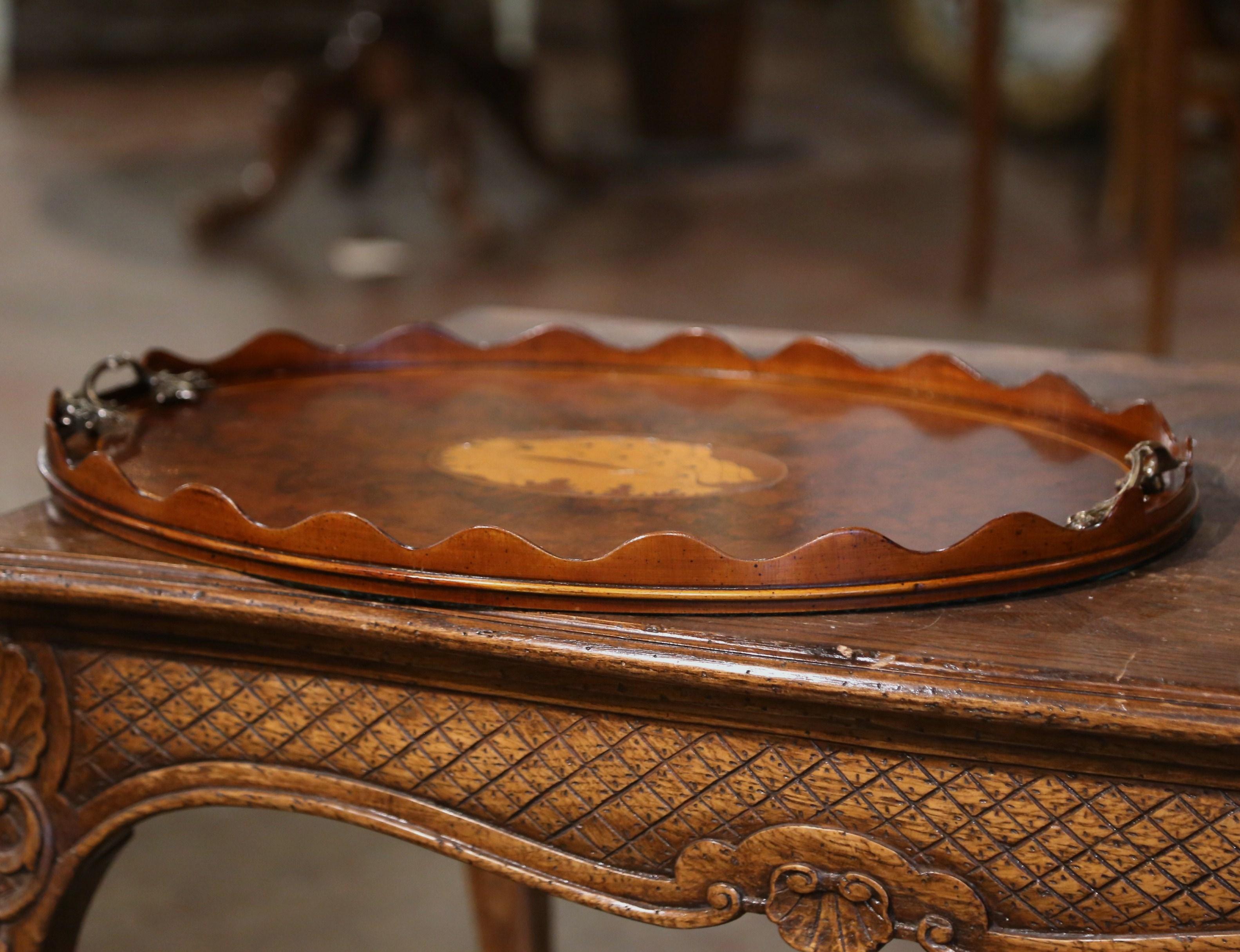 Embellish a coffee table with this elegant antique tray table. Crafted in England, circa 1890 and built of burl walnut, the oval plateau features a raised scalloped edge around the scalloped periphery, and is dressed with two intricate bronze