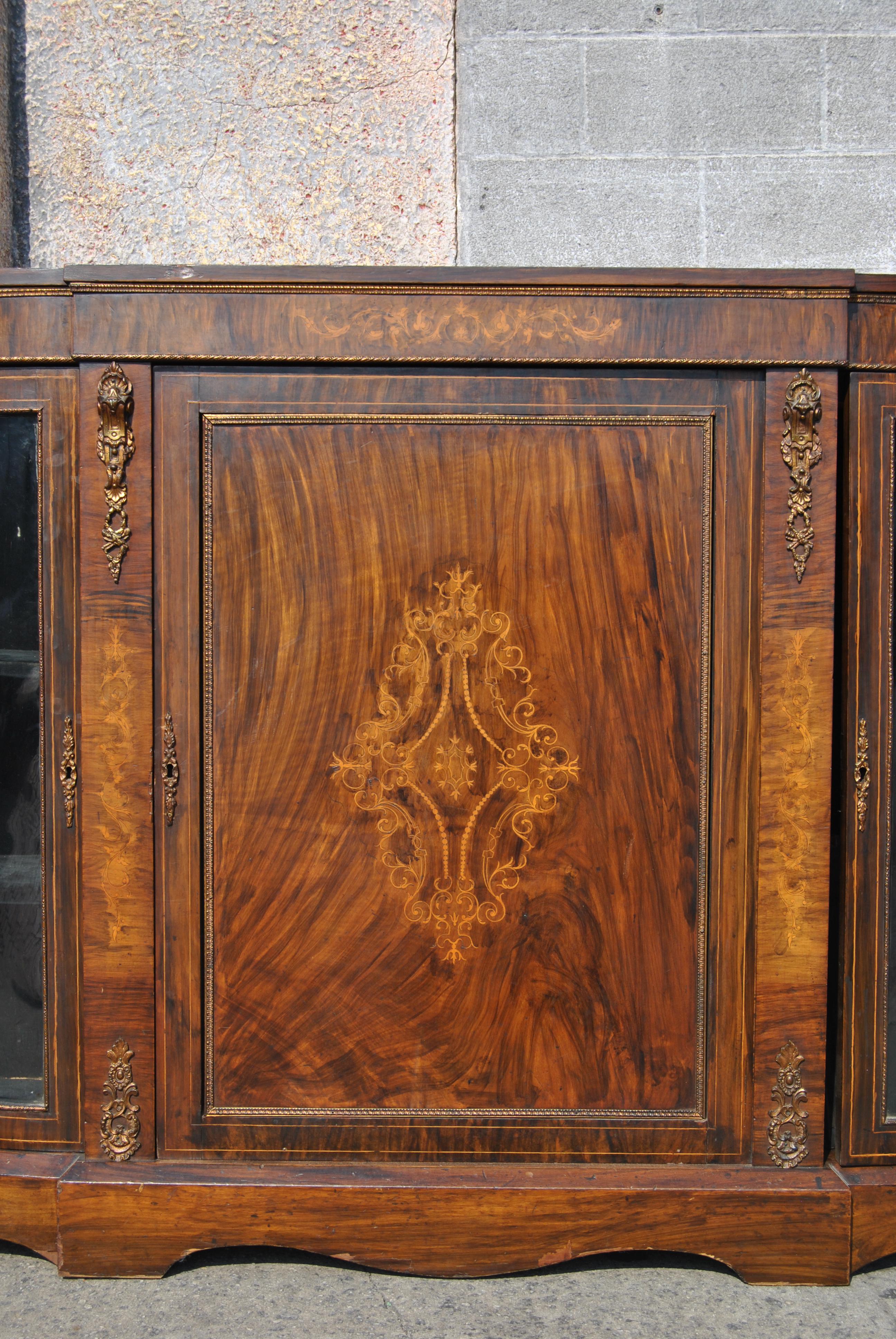 This is a credenza, hall table, side table, server or display cabinet, made in England, circa 1870. It is made of a beautiful, highly figured cut of burr walnut. The cabinet has rounded ends with bowed glass in each of the doors on the right and