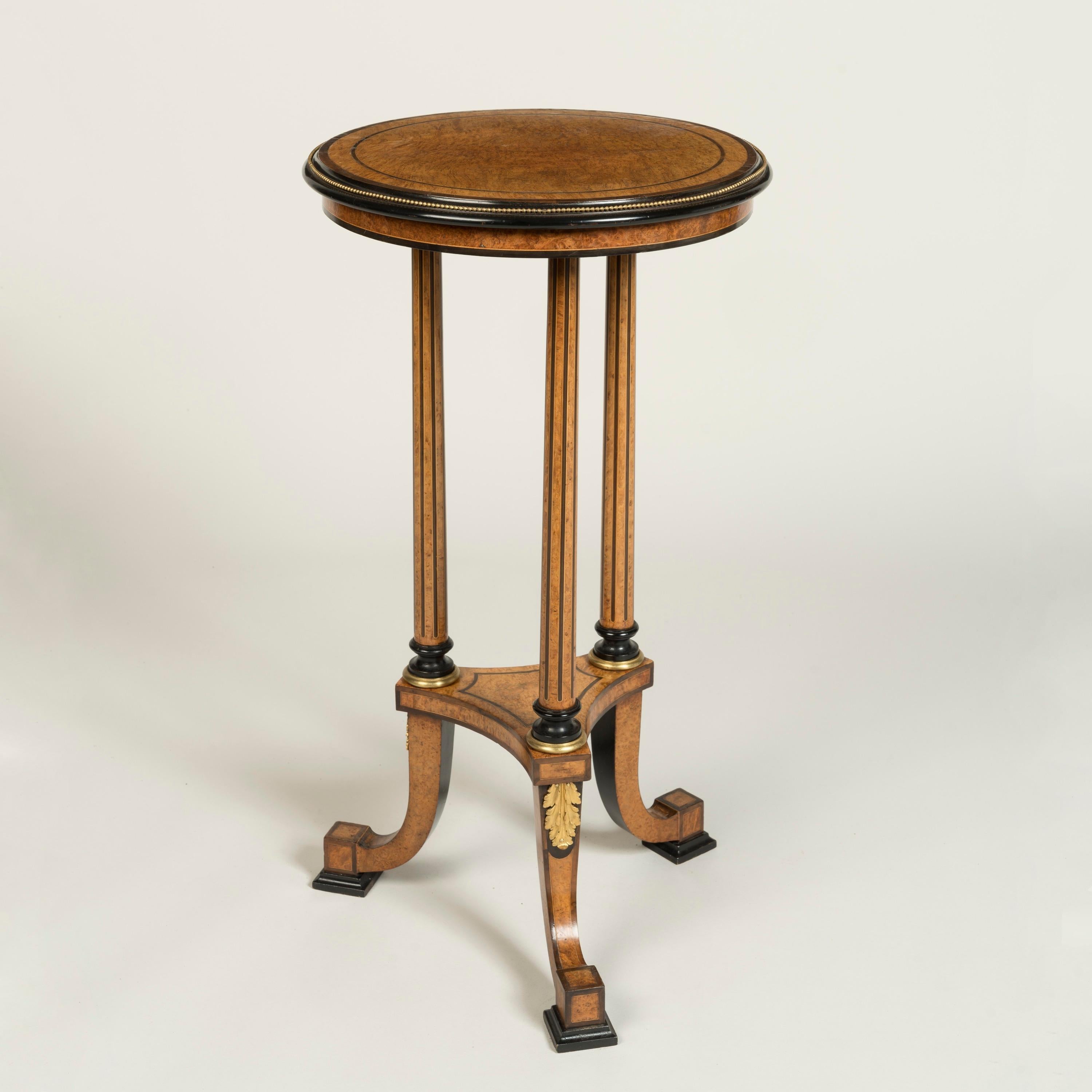 Of beautiful construction from burr walnut, ebony and specimen woods with understated ormolu accents, the tripod table rising from curved legs with rectangular cross-section conjoined by an incurved platform, above emanating three stems with fluted