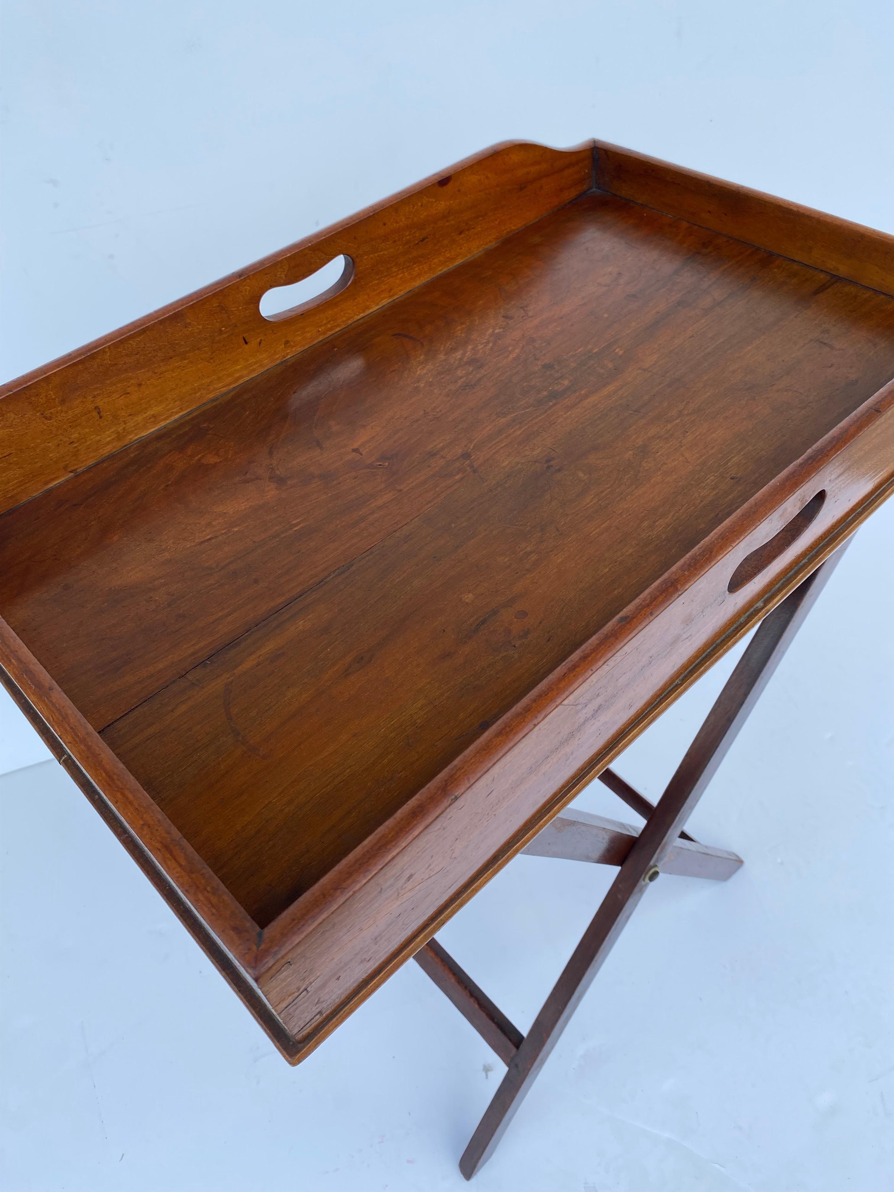A mid-19th century English mahogany butlers tray on the stand features a rectangular tray with a surrounding gallery. On a folding X-frame stand with woven straps to accommodate the tray.