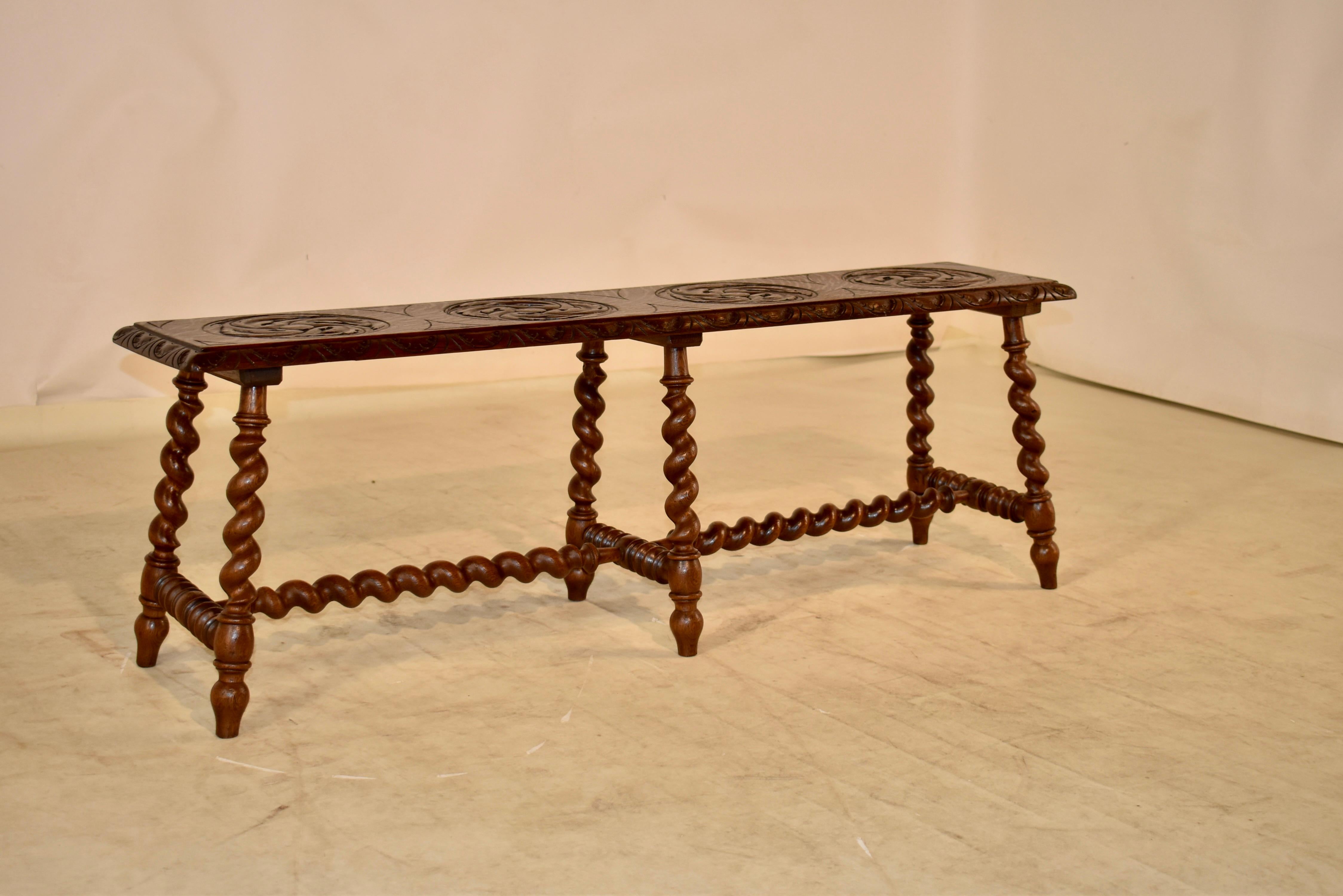 19th century oak bench from England with a single plank seat which has a beveled and carved decorated edge, surrounding a hand carved decorated seat with four lozenges, all carved with acanthus leaf decoration.  the bench is supported on hand turned