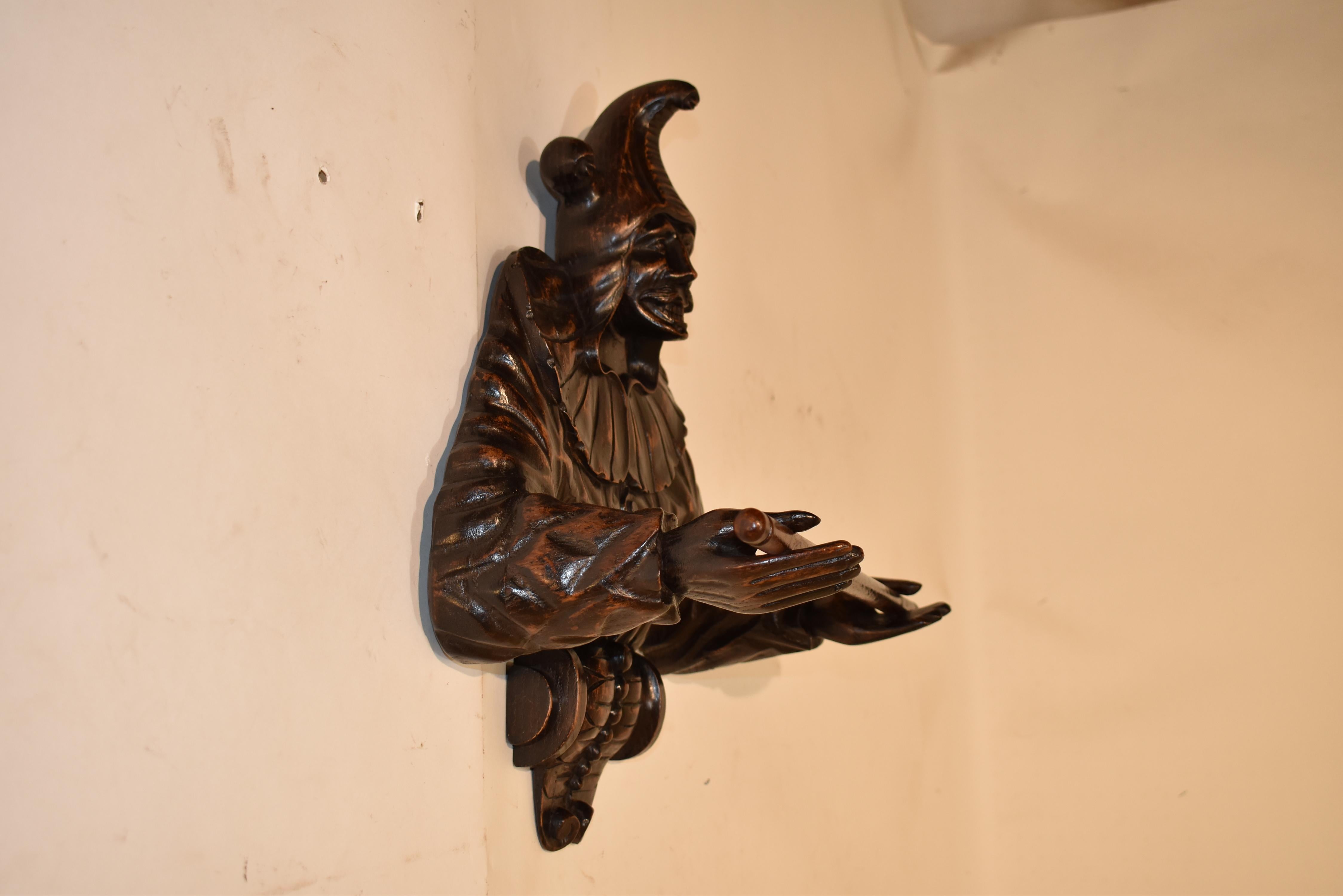 Toallero de madera de frutal del siglo XIX, procedente de Inglaterra.  Esta exquisita pieza está tallada a mano y tiene forma de bufón.  Lleva el típico sombrero de bufón y un volante alrededor del cuello sobre la túnica, con botones por toda la