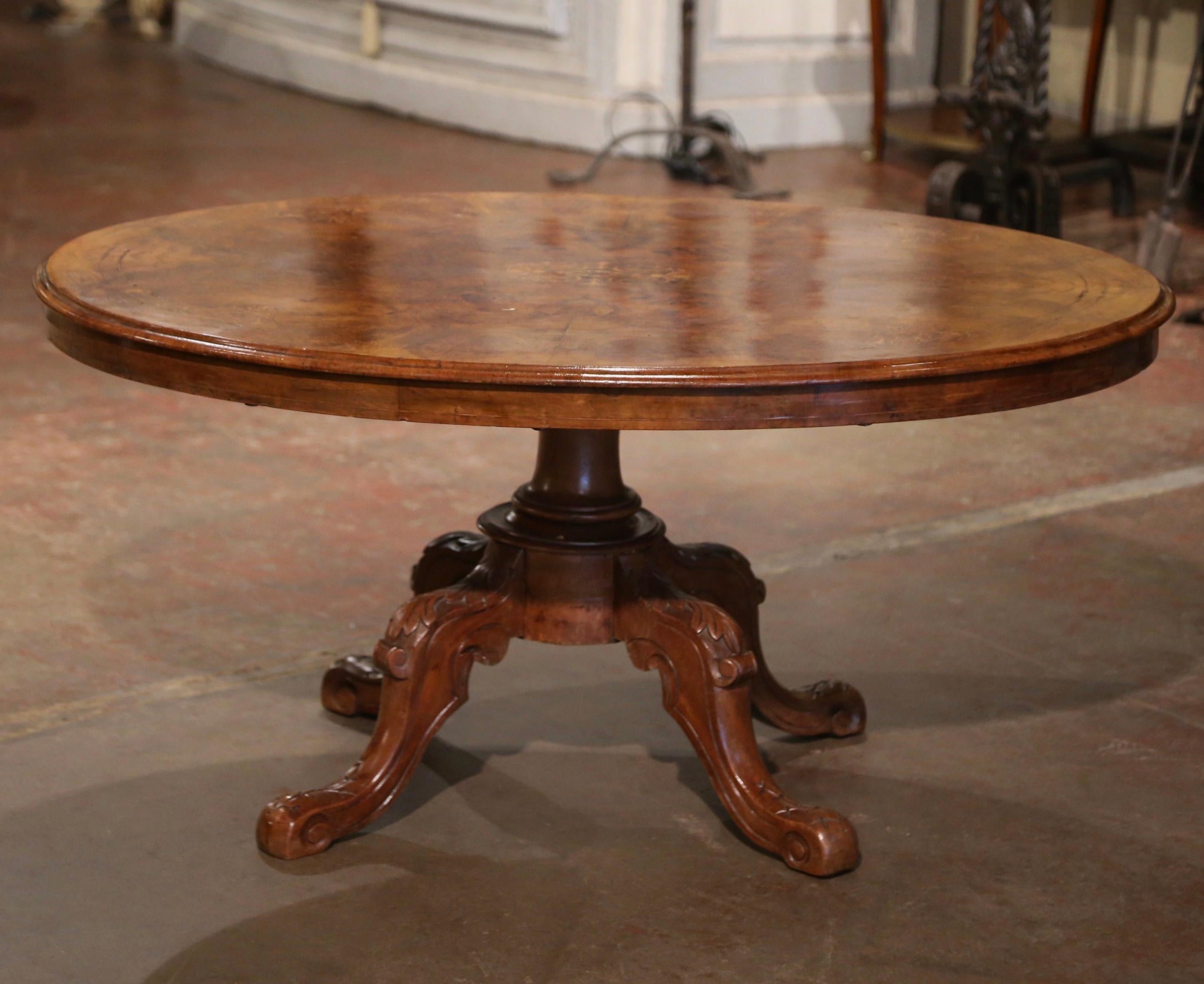 Decorate a den or living room with this elegant antique cocktail table. Crafted in England circa 1860, the large table stands on a center carved walnut stem supporting four curved legs decorated with acanthus leaves and ending in scroll feet. The