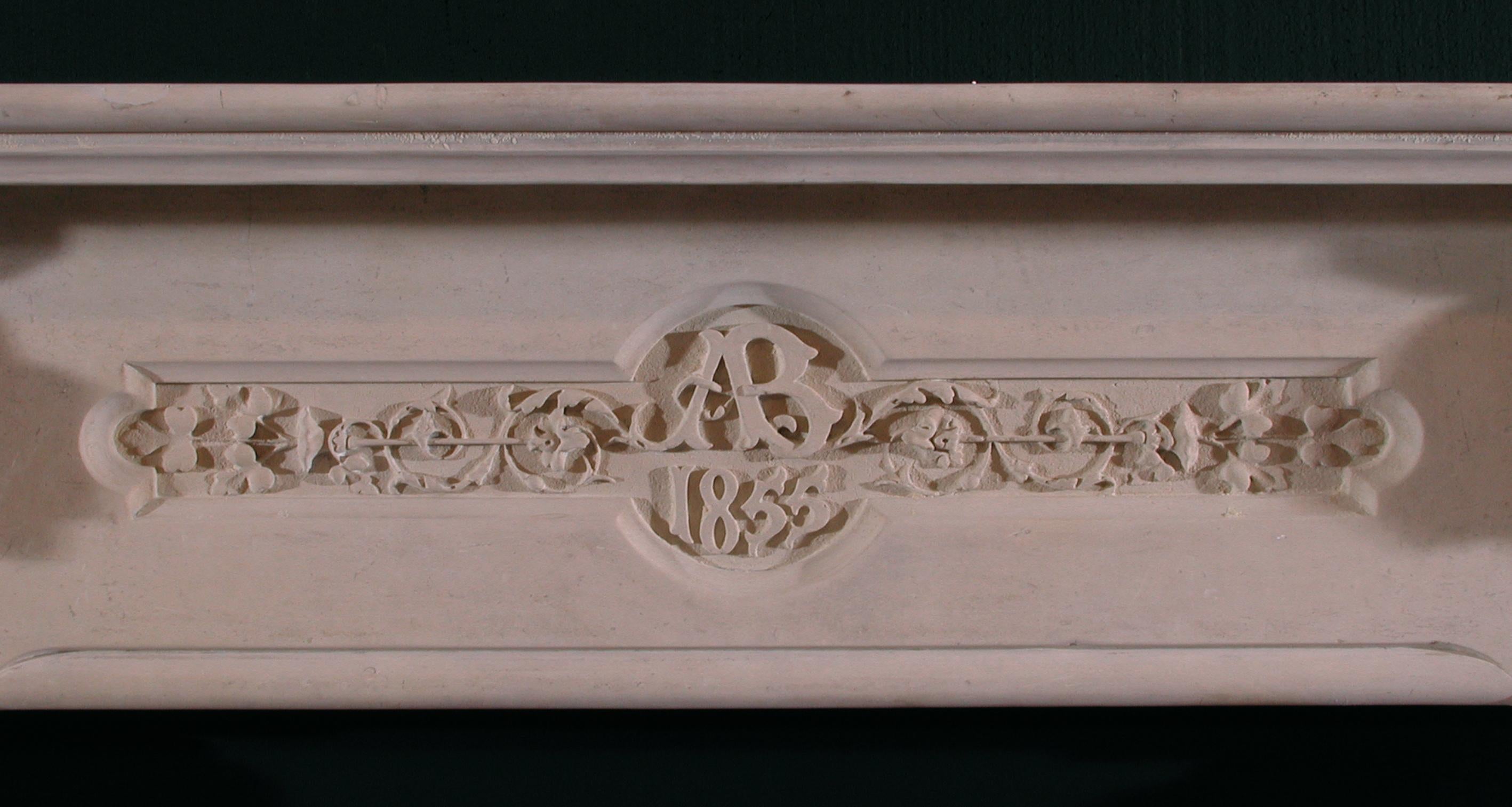 A 19th century English carved limestone fireplace, with the initials 'AB' and the date 1855 carved to the centre of the frieze, jambs carved with bellflowers and ears of wheat, surmounted by carved male and female faces.

 Shelf Width:	1905 mm     