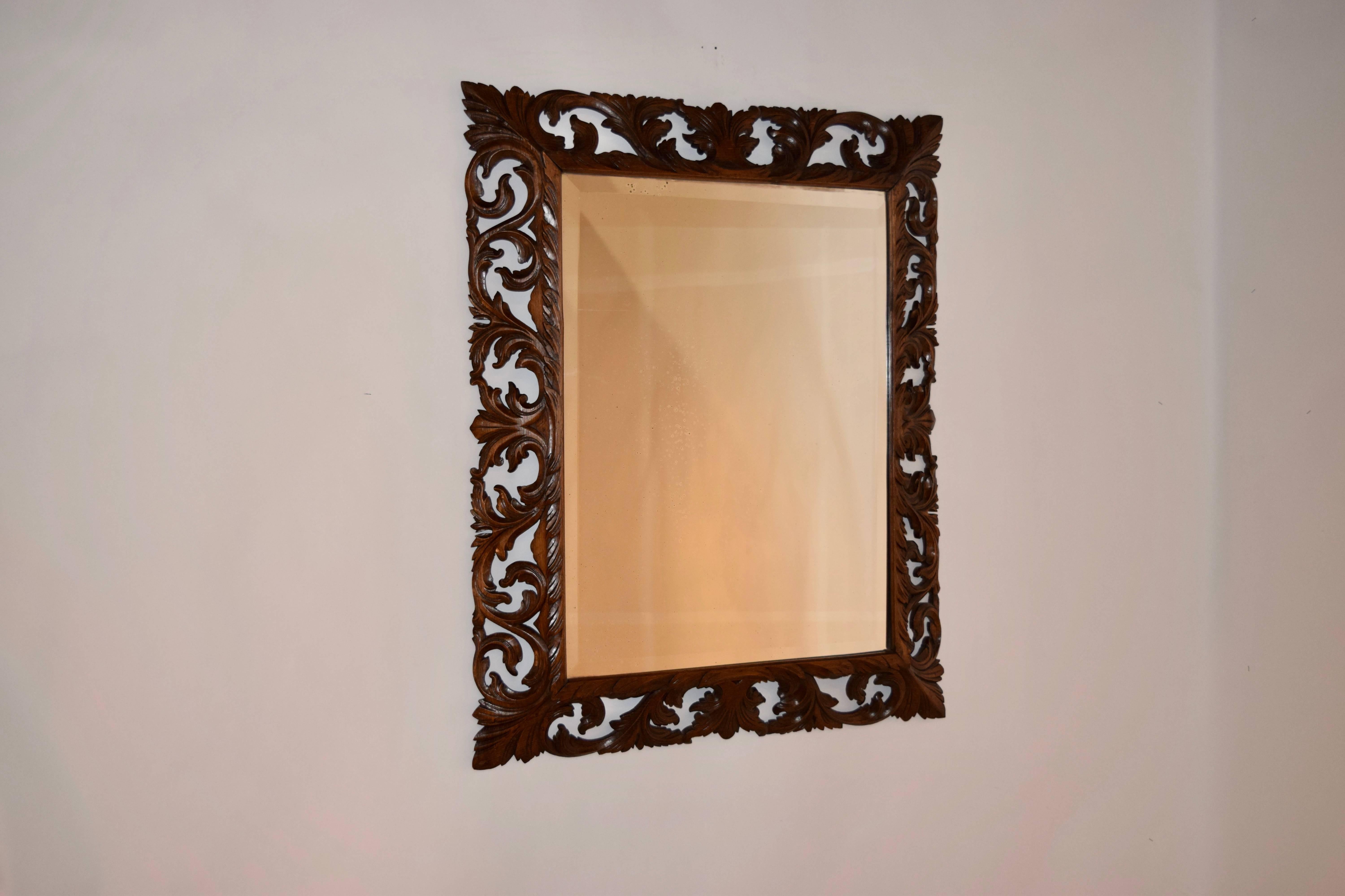 19th century English hand-carved frame with a border of leaves and scrolls, surrounding a beveled mirror.