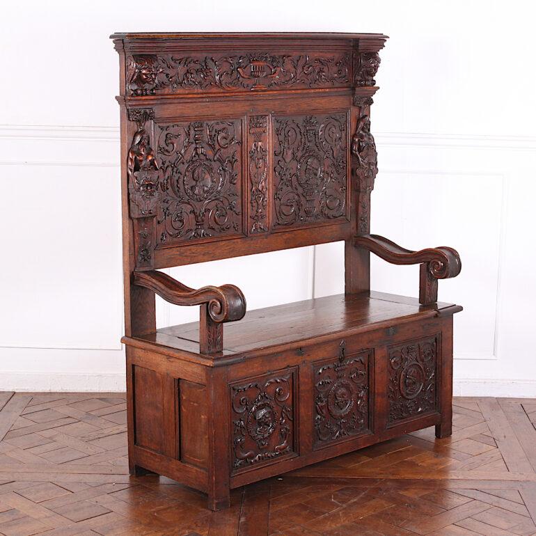Highly carved English Renaissance revival oak hall bench, the tall back with exceptionally-finely carved classical motifs- swags, folliage, urns etc. Figural carvings to each side of the back above boldly-shaped scrolled arms. Paneled base with