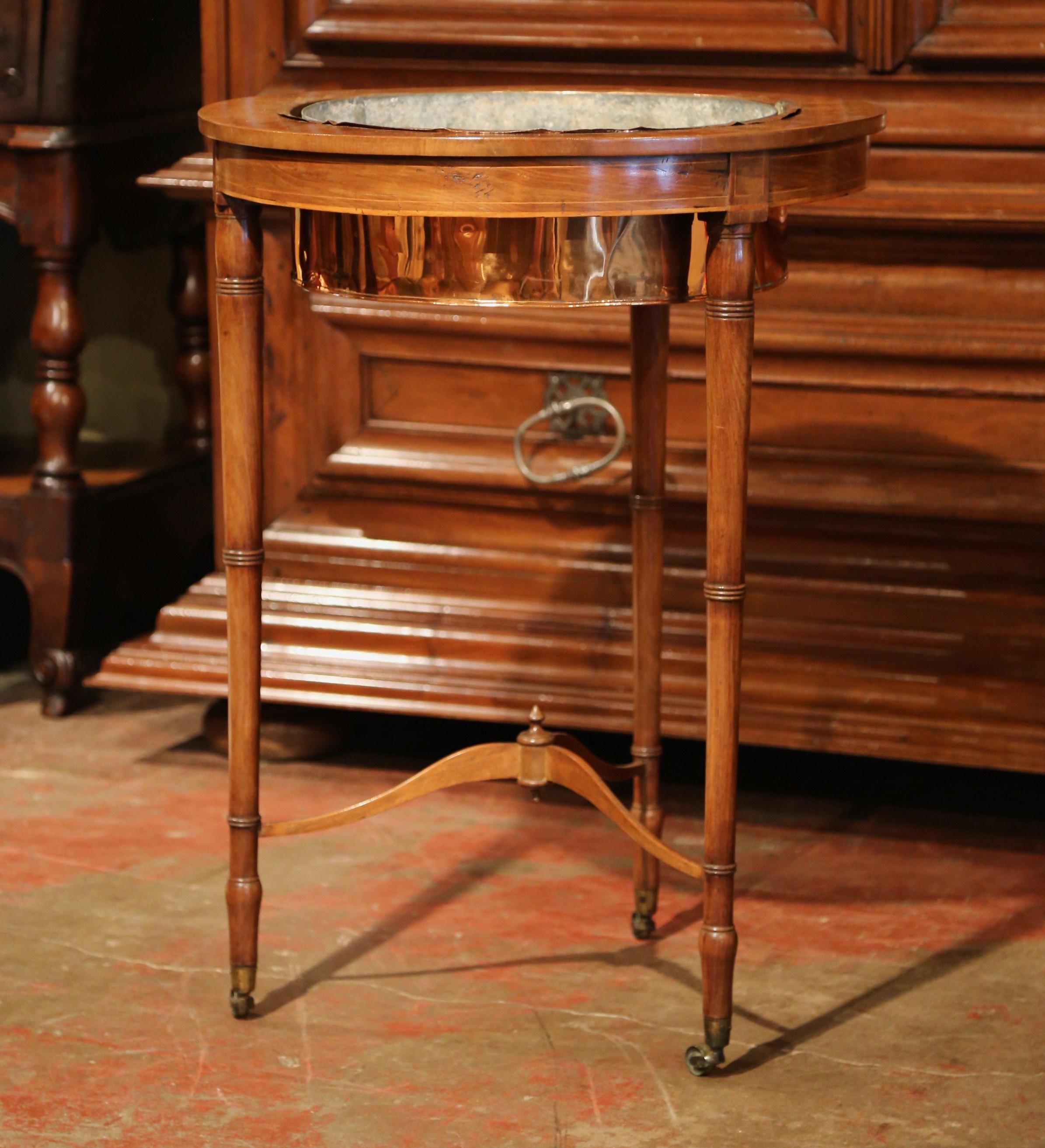 This traditional planter was crafted in England, circa 1880. Round in shape, the plant stand sits on three turned legs with brass wheels and a bottom stretcher embellished by a carved central finial. The plant stand has a removable zinc liner inside