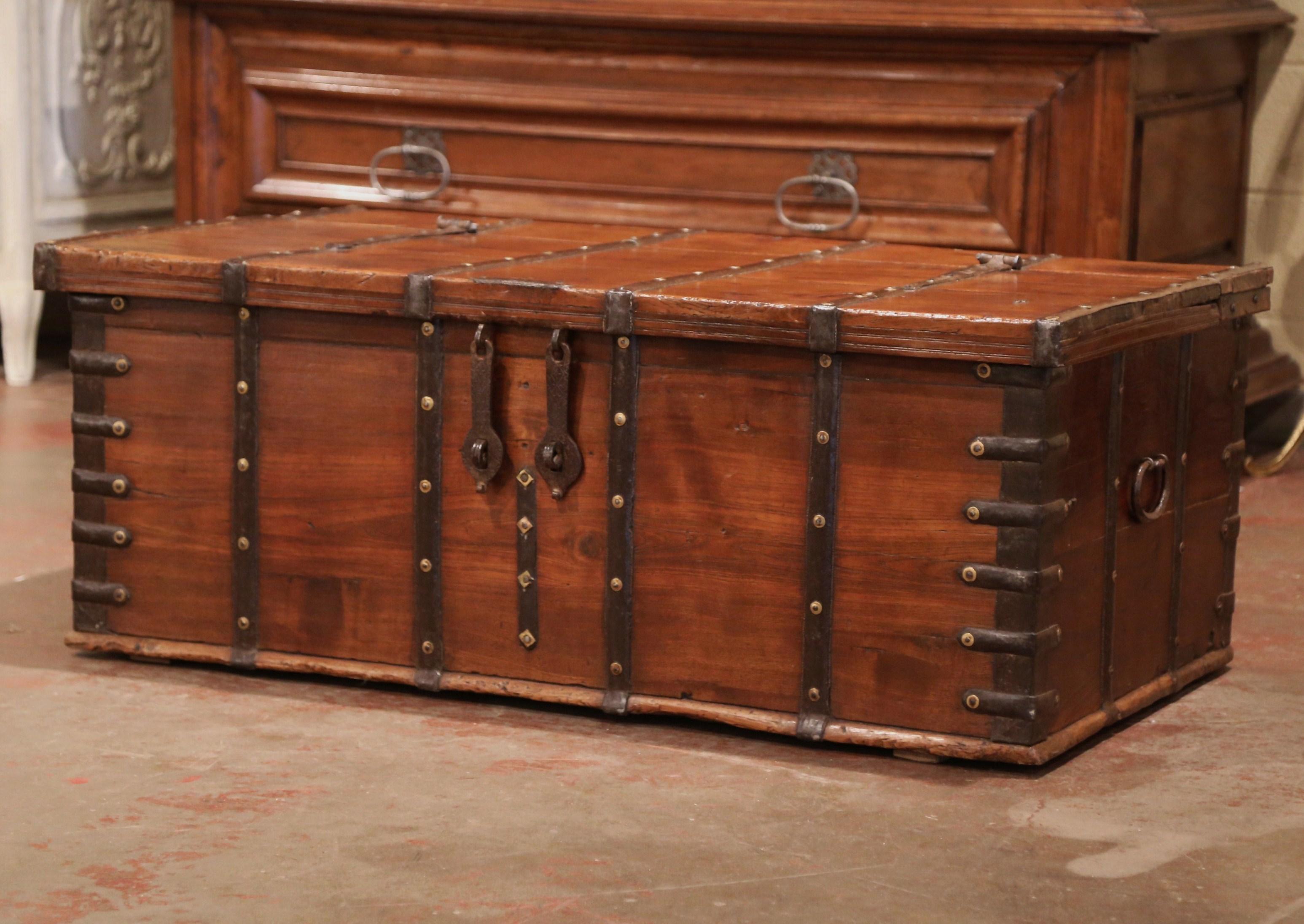 This large antique fruitwood coffee table trunk was crafted in England, circa 1870. The wooden blanket chest is finished on all four sides, and is decorated with metal strapping with decorative brass nail heads; it is further embellished with