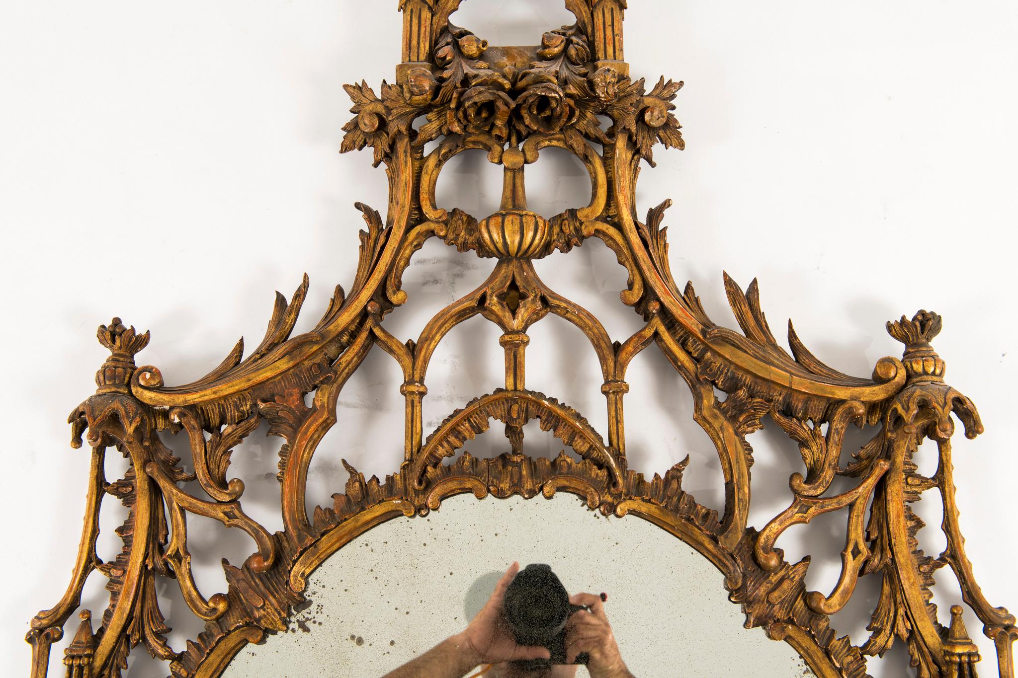 A 19th century English Chippendale giltwood mirror. This Classic chinoiserie style mirror is besieged with a mix of roses, foliage, fretwork, columns and gabled roofs.
