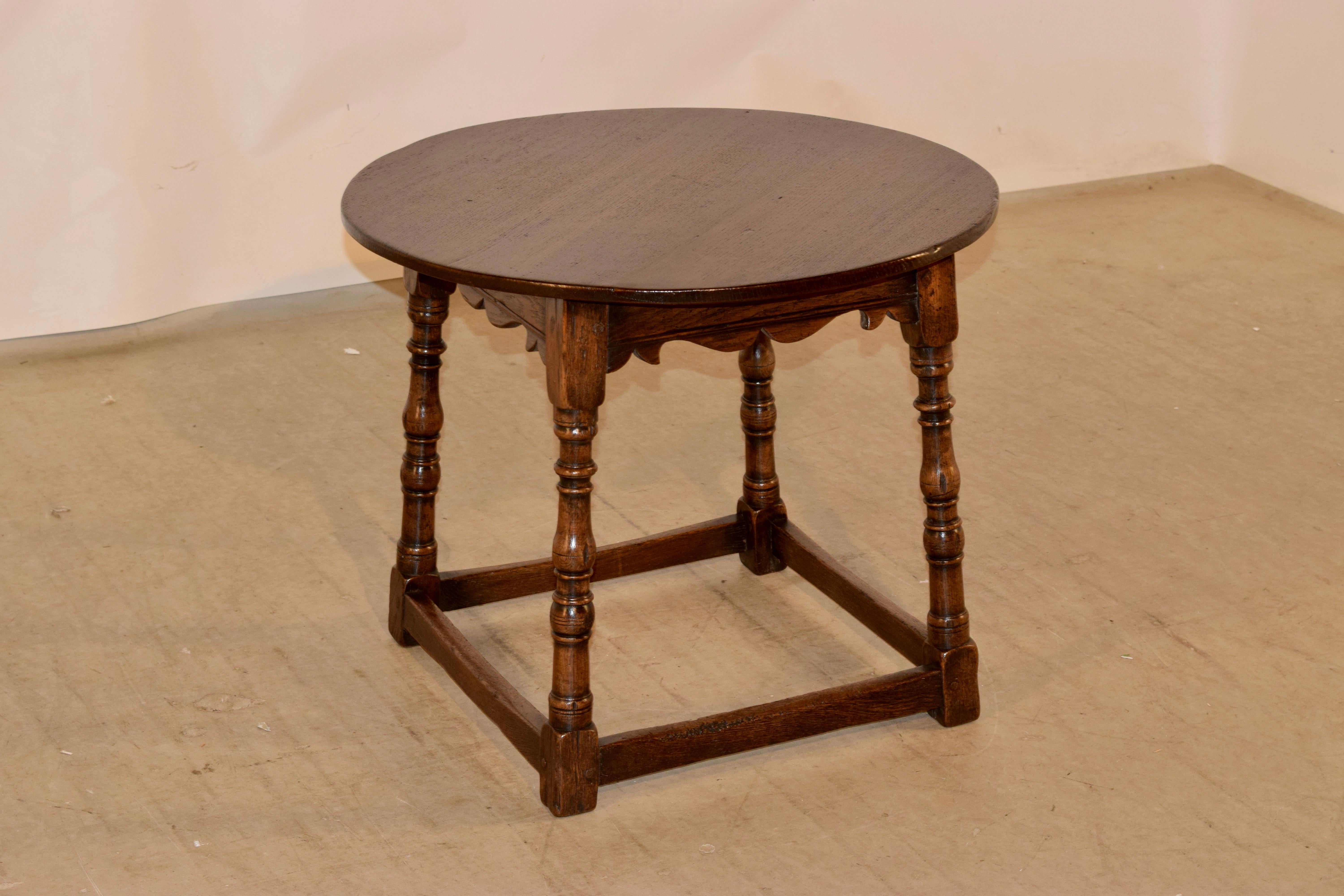 19th century oak cocktail table from England with a round top over a molded and hand scalloped apron and hand turned splayed legs, joined by simple stretchers.