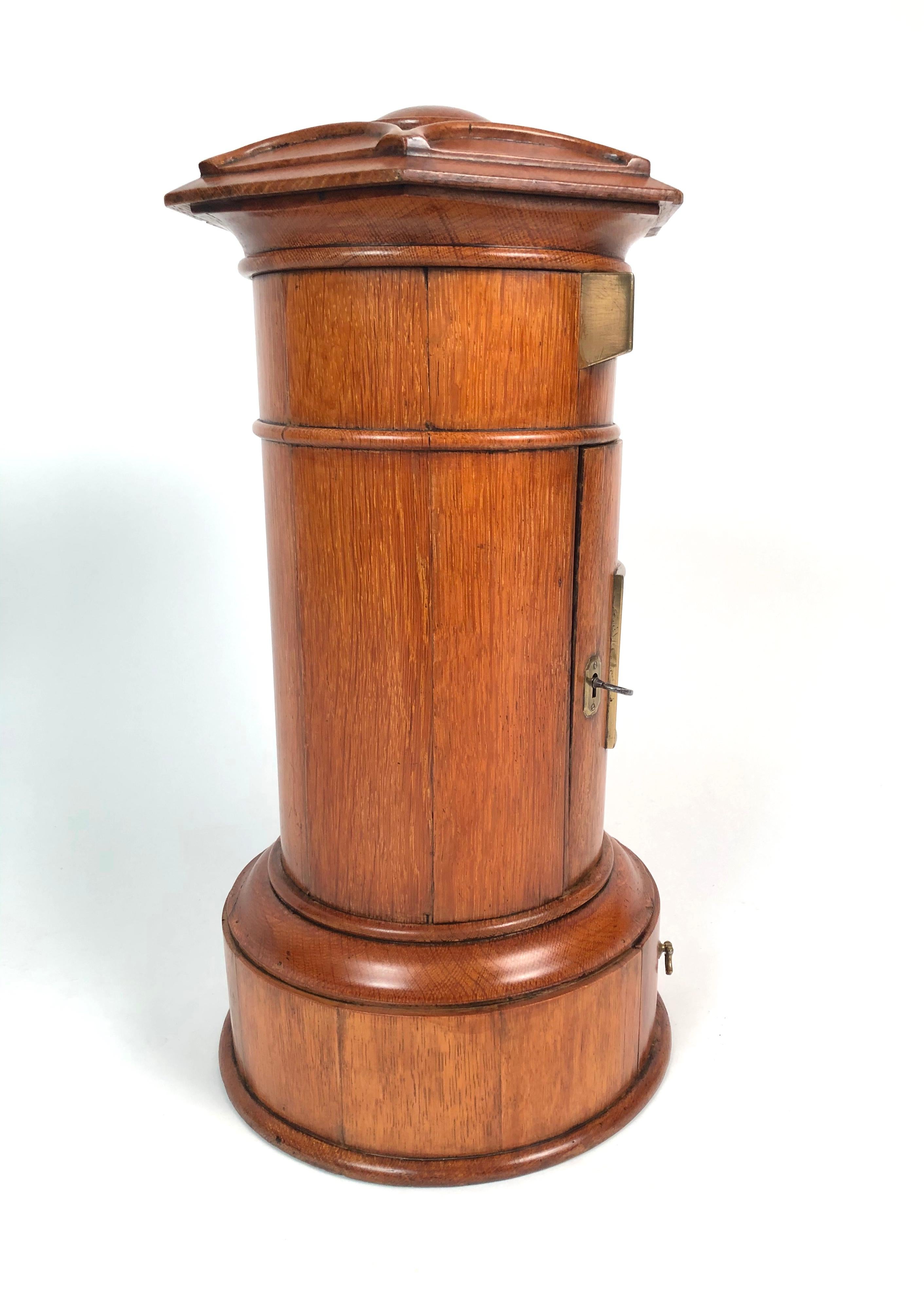 A charming and finely made English Victorian country house Royal Mail letter box of typical pillar form with octagonal top in golden oak, with brass letter slot, locking door with handwritten schedule of Royal Mail collection times, and drawer