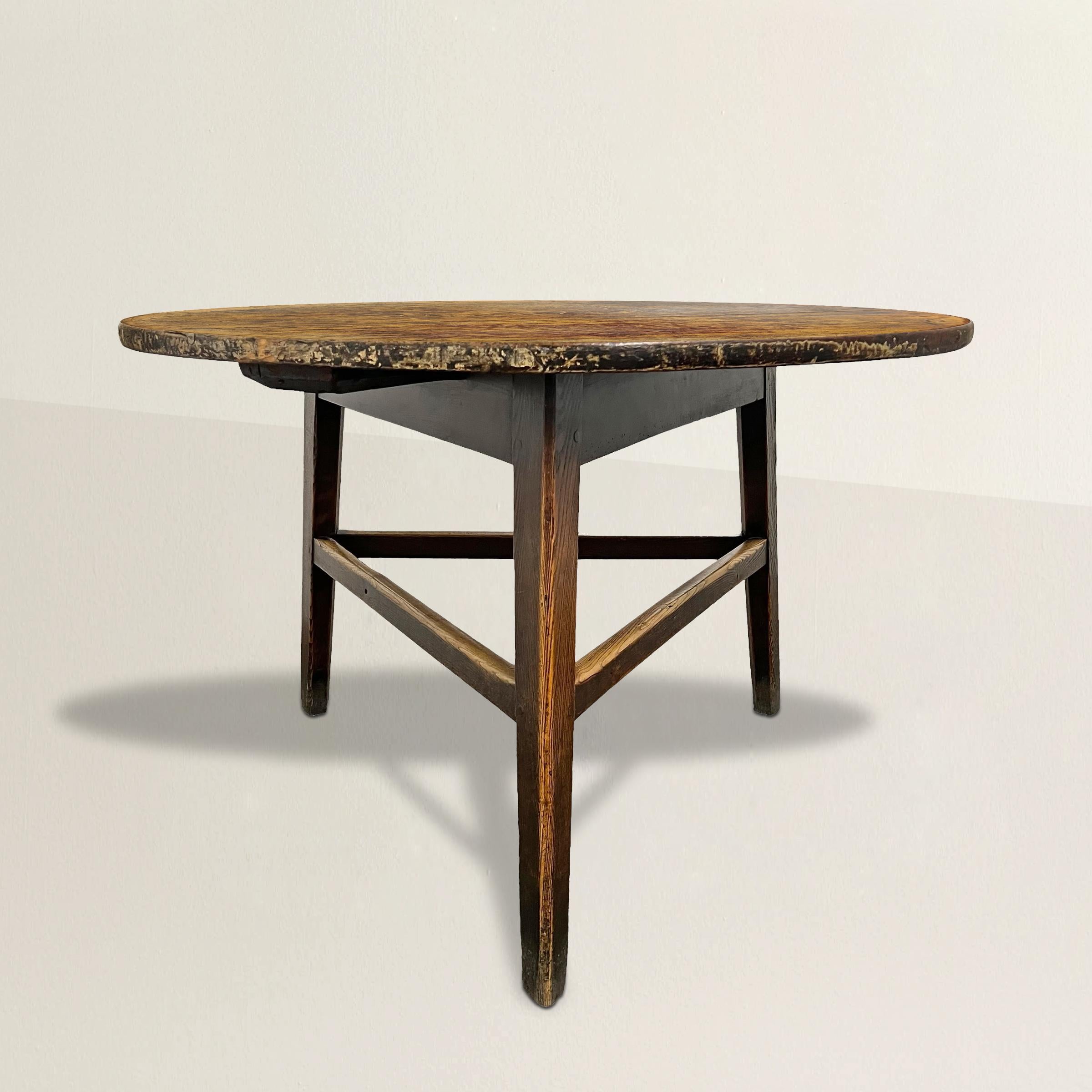 Standing as a testament to 19th-century English craftsmanship, this exceptionally large cricket table is a captivating piece of furniture. Its round top boasts a patina that tells the tale of years gone by. Supported by three elegantly tapered legs,