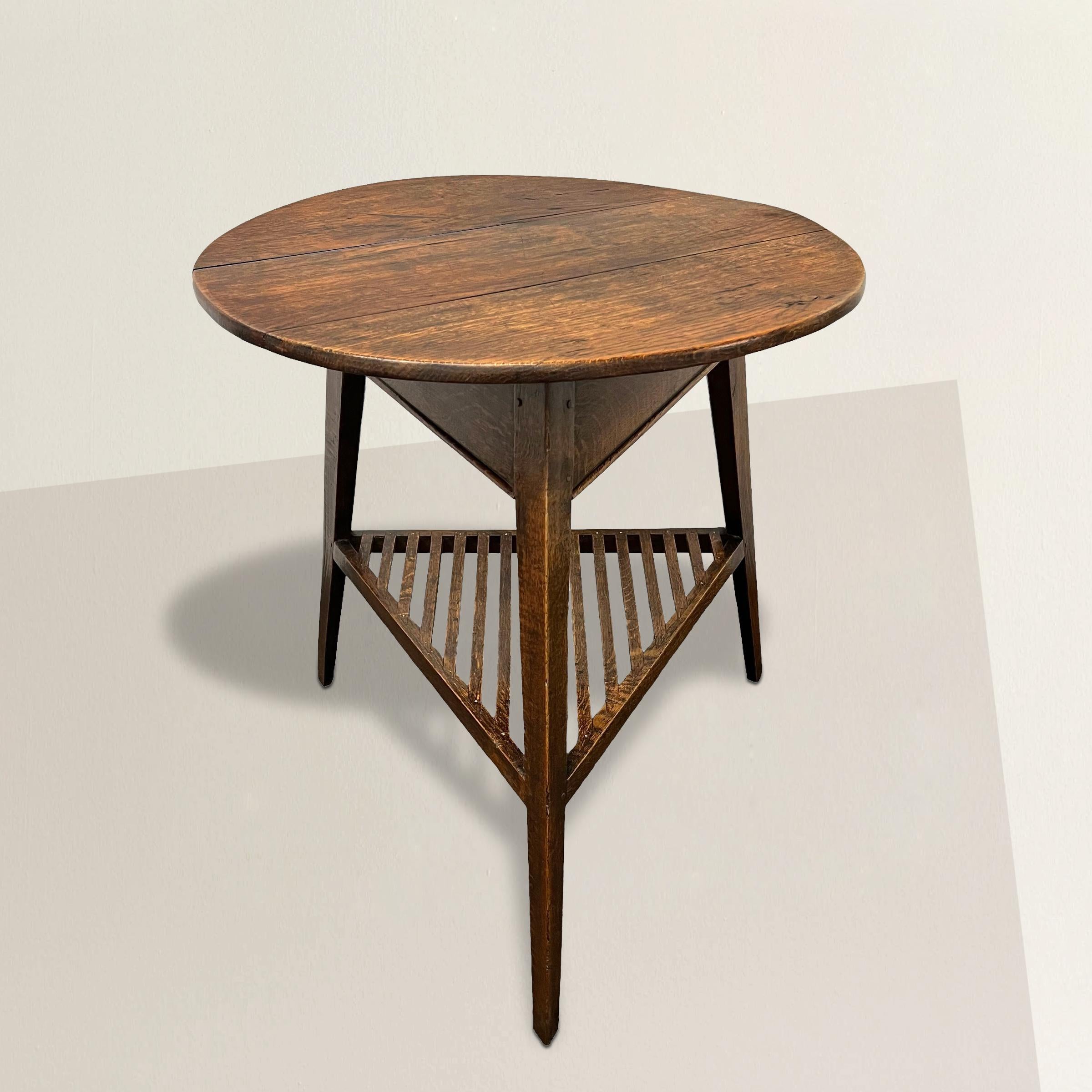 This early 19th-century English oak cricket table epitomizes the charm and functionality of its era. Crafted with meticulous attention to detail, its round top exudes a rustic elegance, while the lattice shelf below adds both practicality and