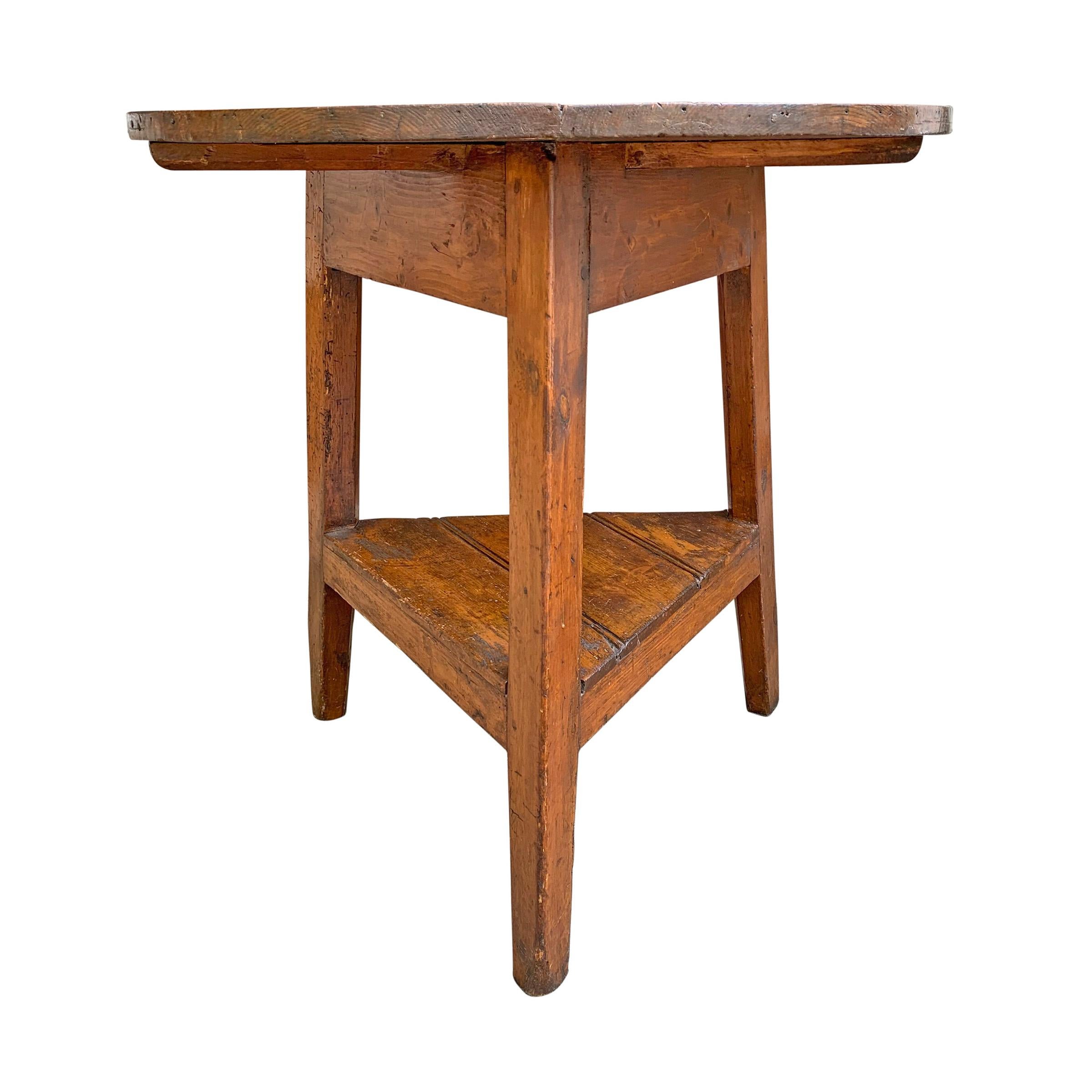 A fantastic 19th century English pine cricket table with three legs, a round top constructed of two pieces of wood, and a bead-board shelf on the bottom. Fantastic color!