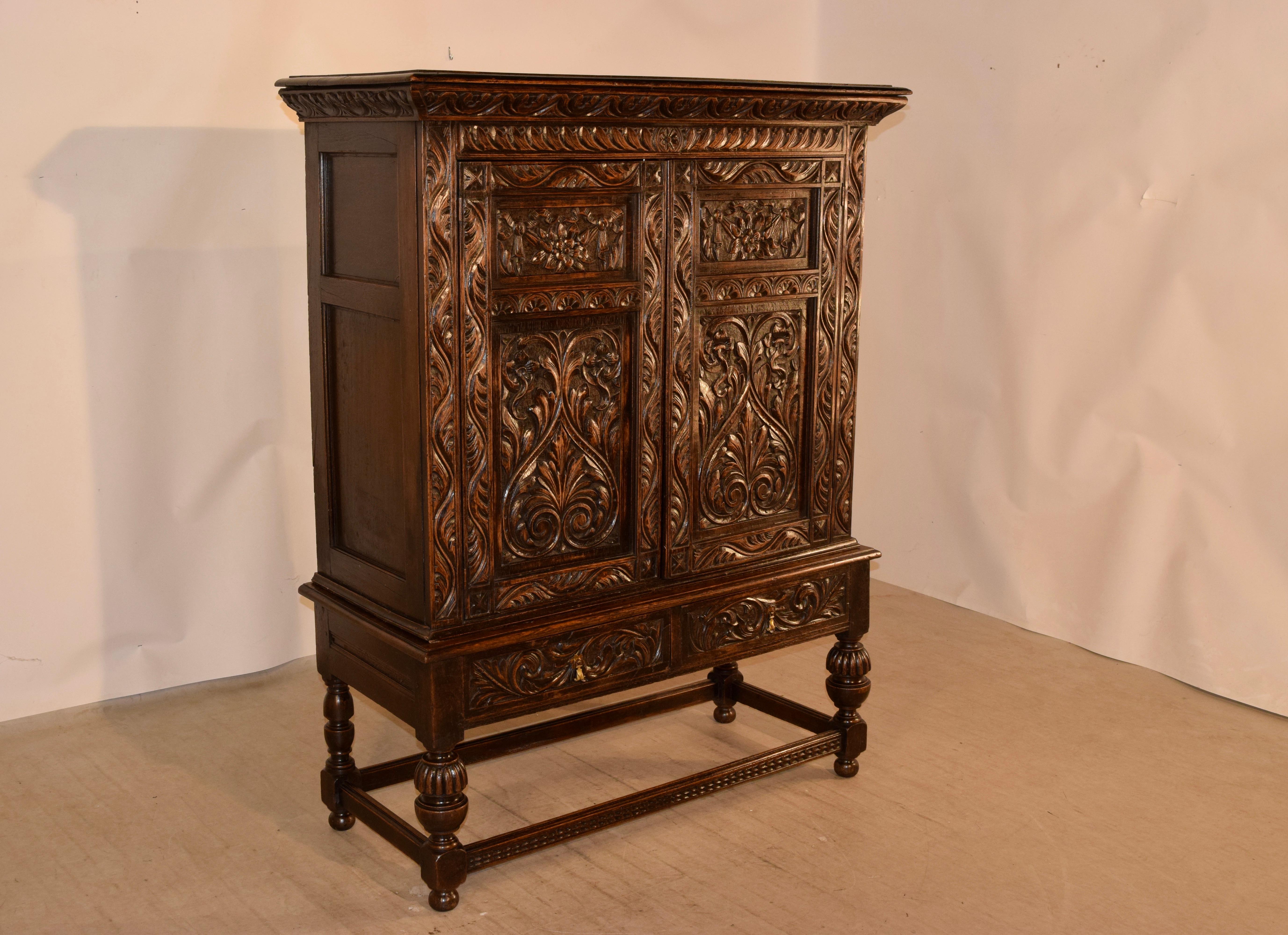19th century English oak cupboard on stand with a lovely hand carved decorated crown over paneled sides and two carved and paneled doors on the front. The doors open to reveal serpentine shelving. The top rests on a base with paneled sides and two