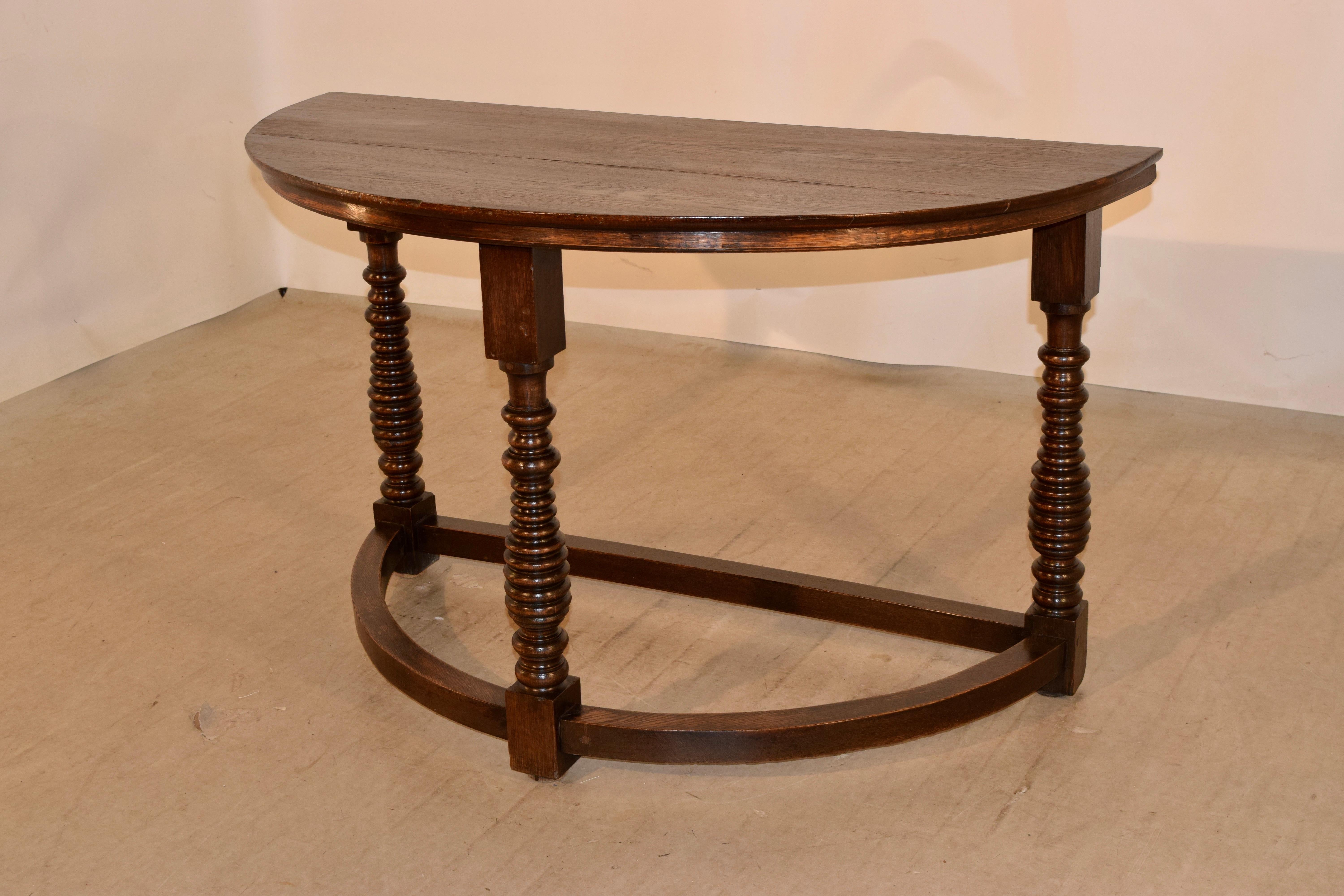 19th century English demilune table made from oak. The top is made from two boards, and follows down to a simple apron. The table is supported on hand-turned graduated beehive shaped legs, which add interest. The legs are joined by simple curved